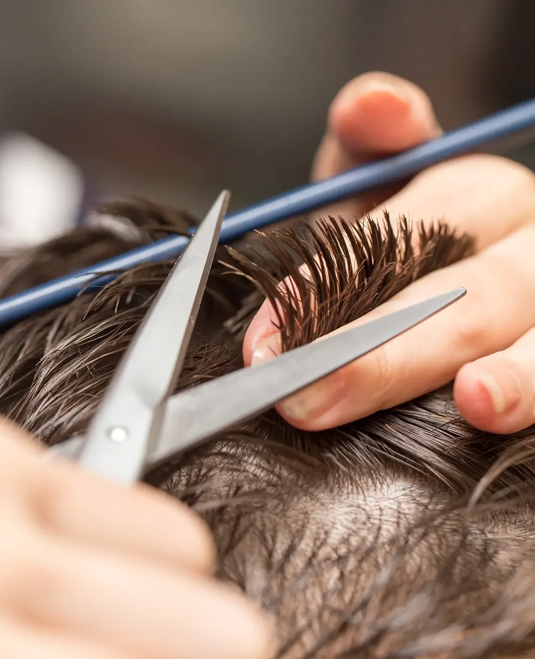Close-up of stylist’s hands holding short hair with scissors, ready to trim.