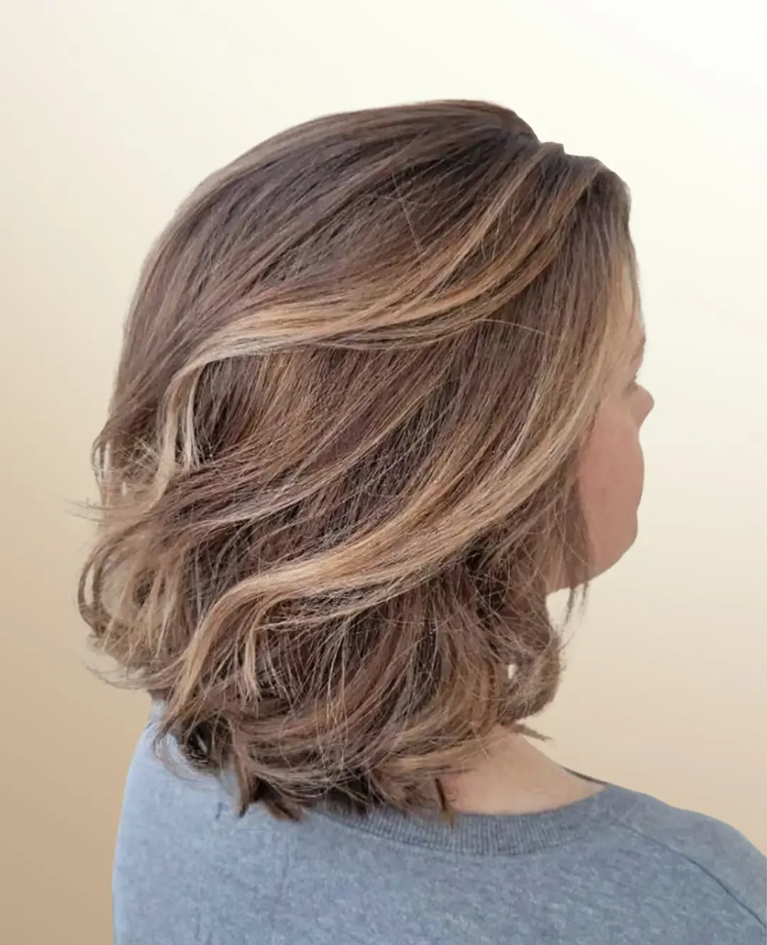 Woman with fresh shoulder-length haircut, soft highlights and loose curls.