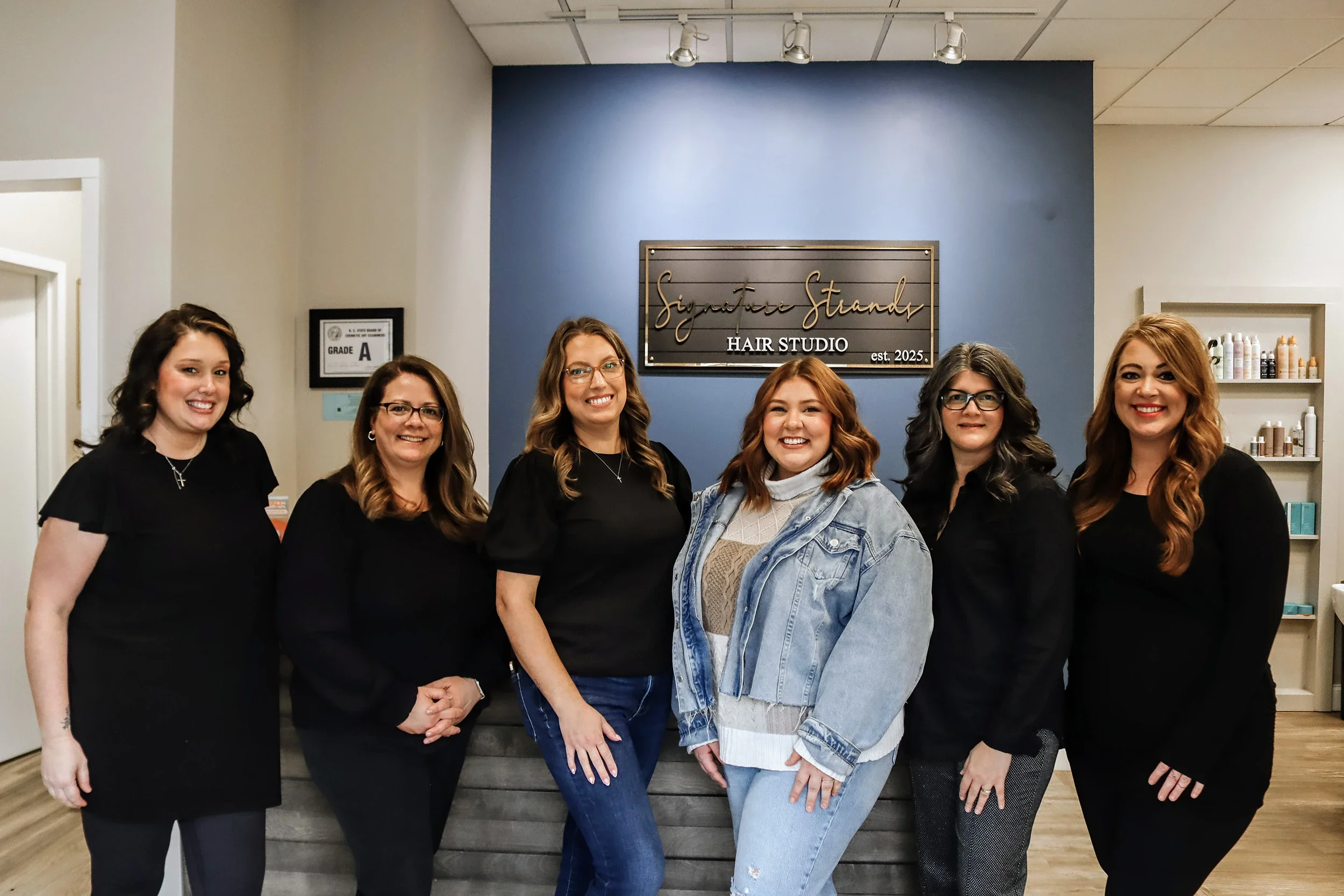The hair stylists standing in front of the Signature Strands sign.