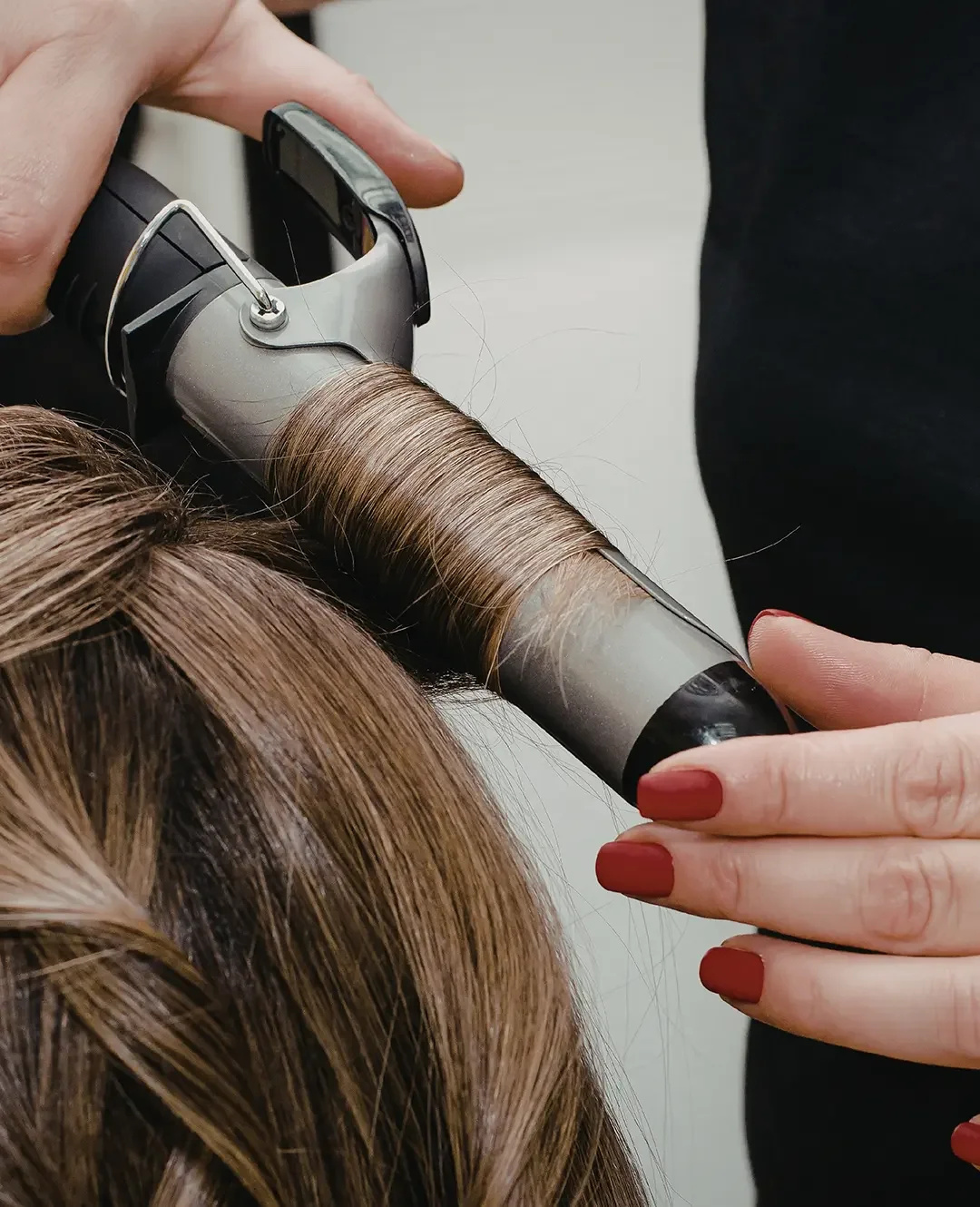 Stylist using a curling iron to style a client's hair after a blowout.