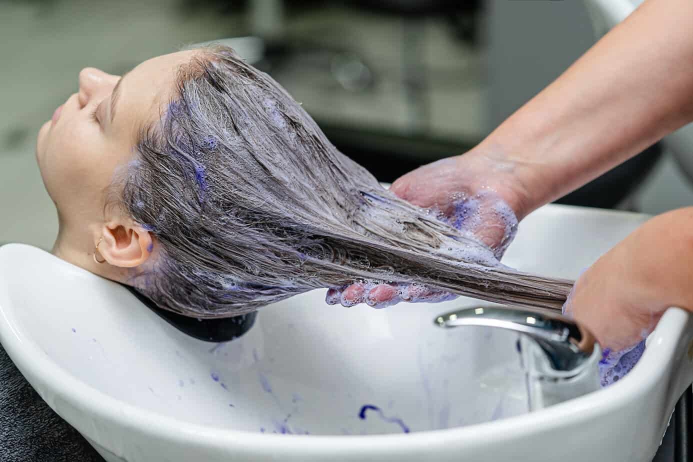 Woman receiving a purple shampoo wash following a professional hair color treatment.