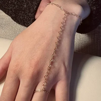 Close-up of a hand with a delicate chain bracelet that drapes to form a T shape, with a textured fabric in the background.