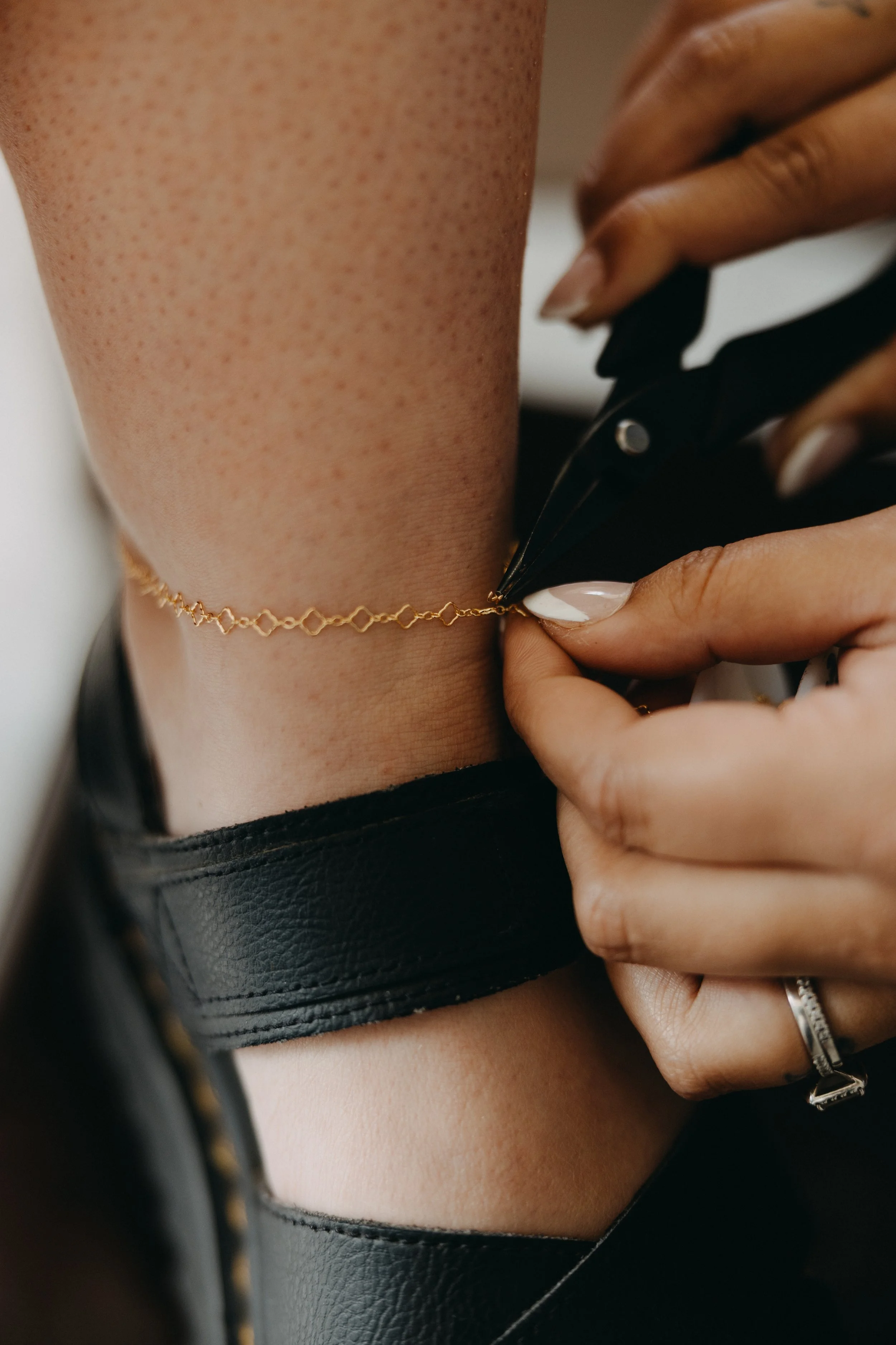 Close-up of a person’s legs resting on a surface, wearing sheer stockings and a delicate gold anklet.