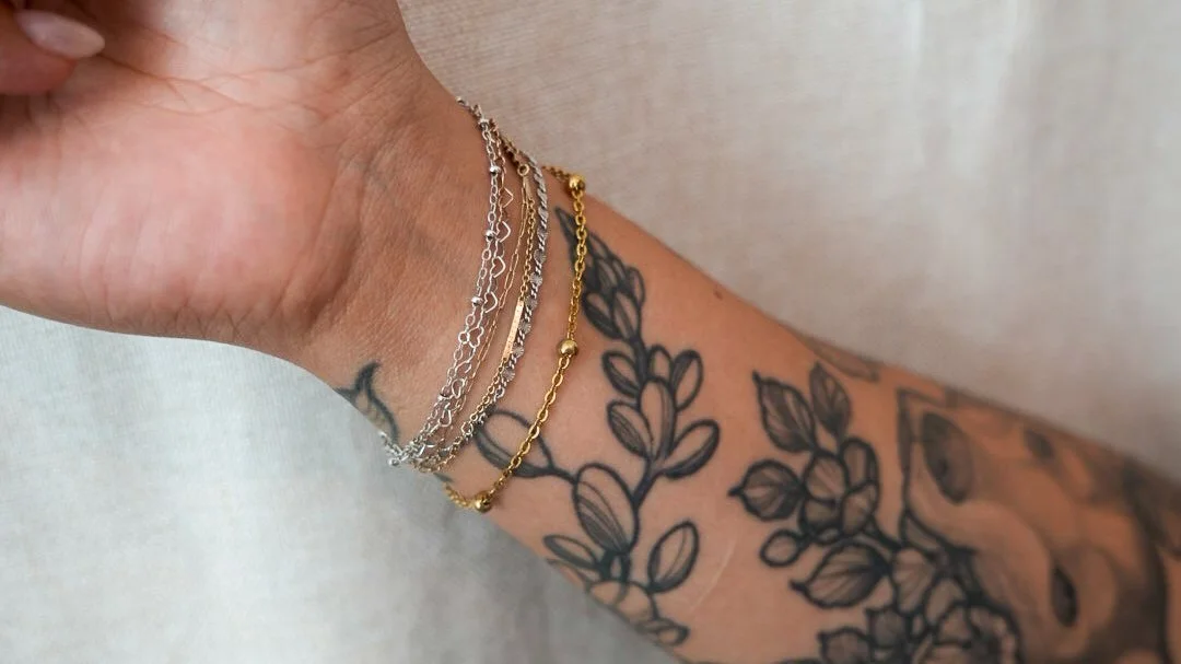 Close-up of a person's wrist with a tattoo and a silver bracelet that spells 'auntie'