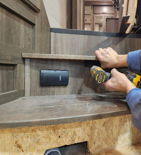 Mobile repair technician using a yellow power drill on a wooden stair step in an RV as part of a manufacturer recall notice for repair and replacement.