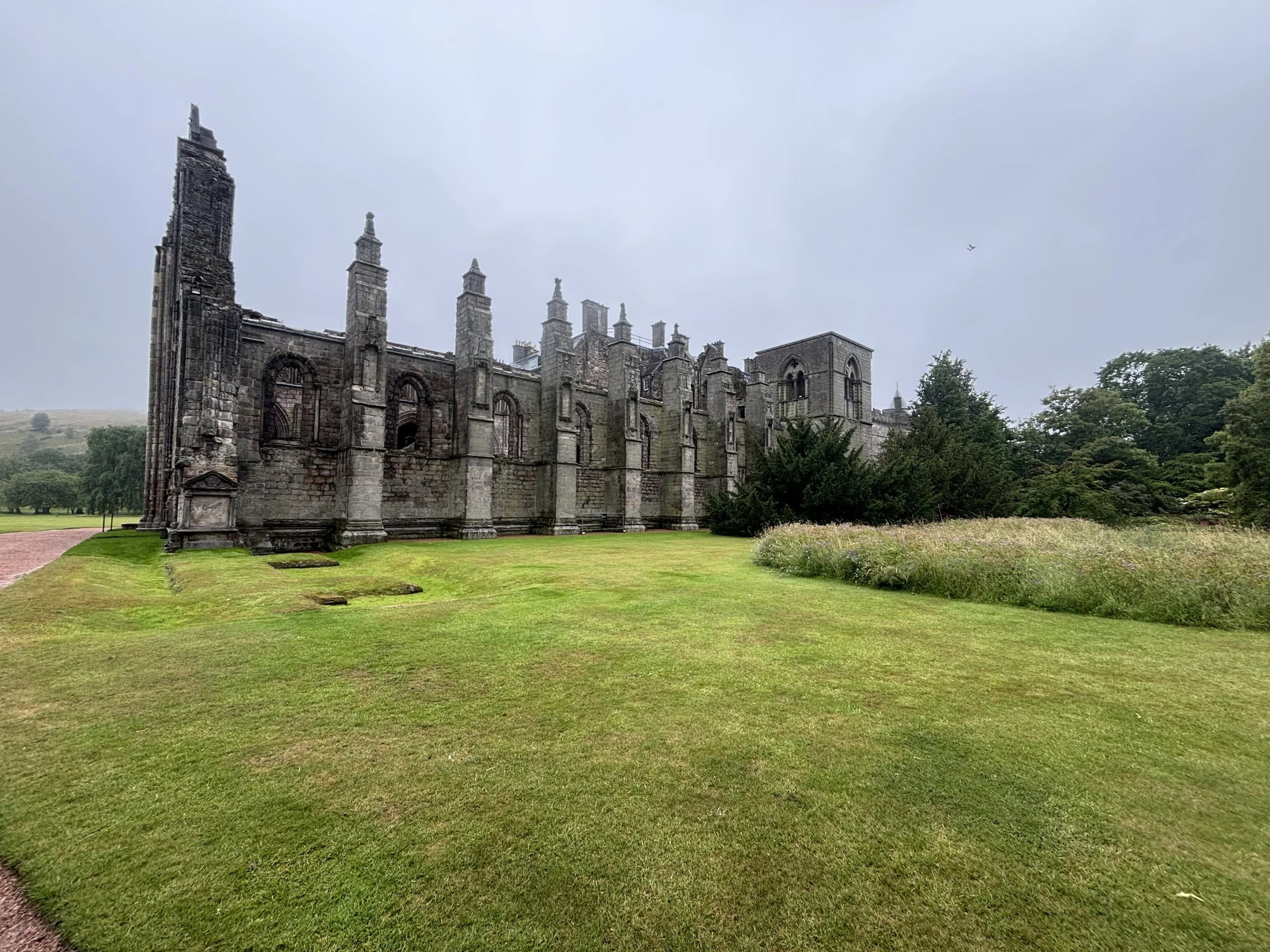 Ruined stone church with arched windows, surrounded by a well-maintained lawn and trees, under a cloudy sky.