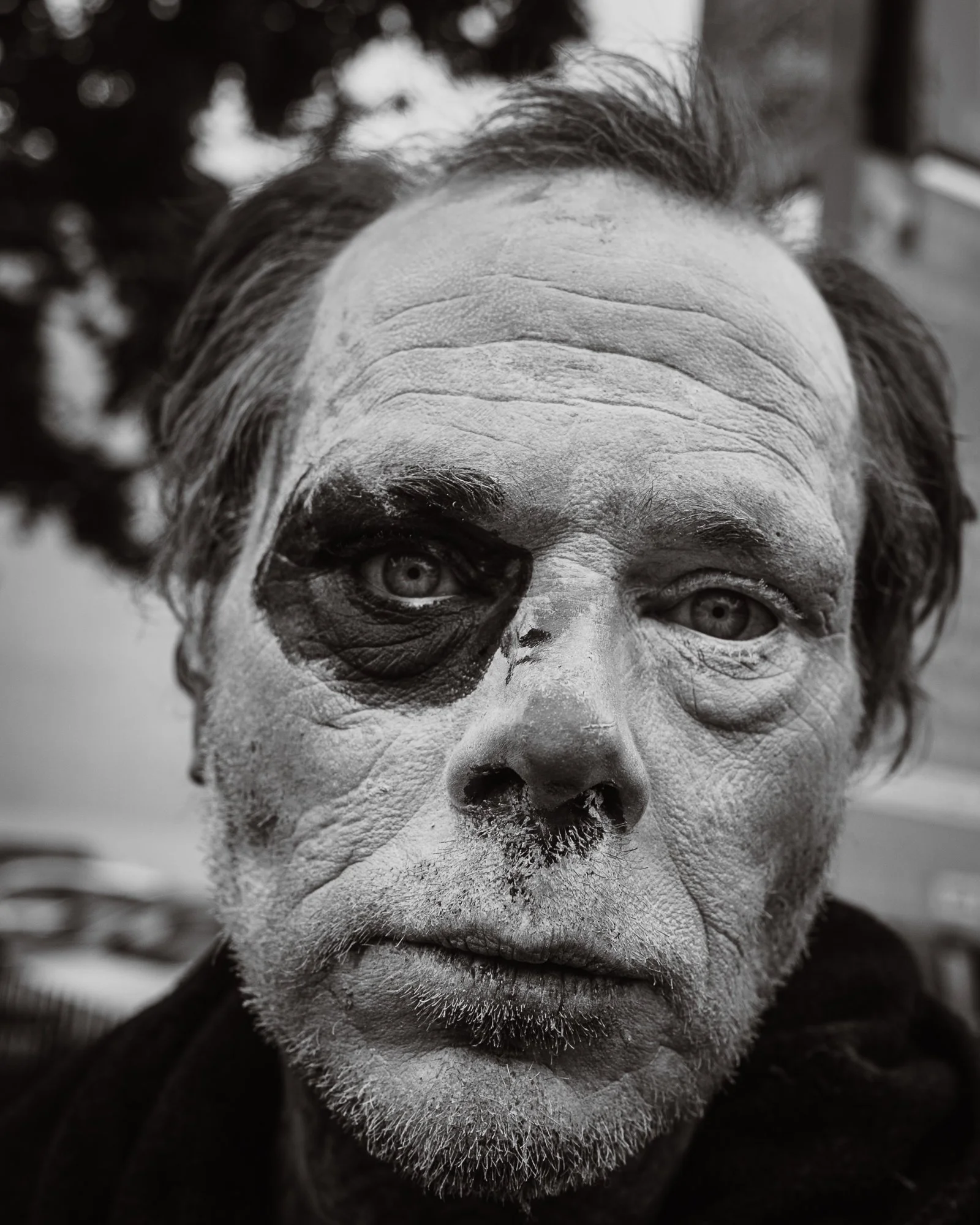 Close-up of a man's face with white face paint, black eye makeup, and elaborate hairstyling