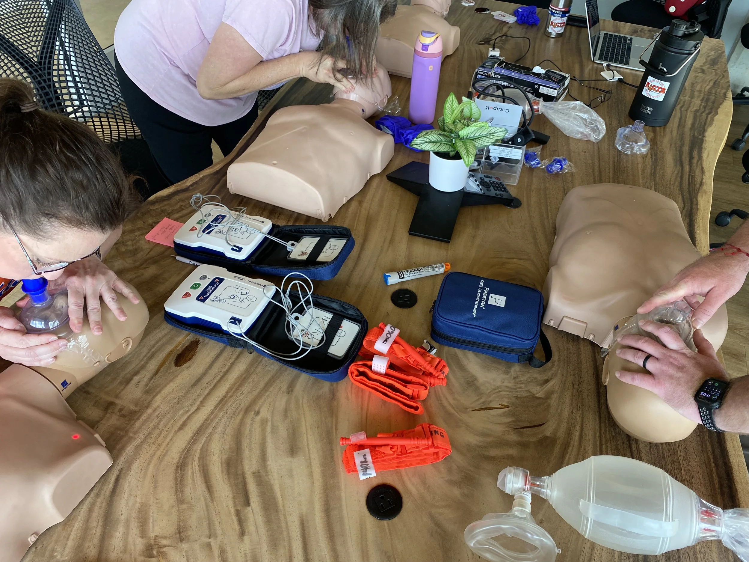 Two participants practicing rescue breathing techniques using pocket masks on adult CPR manikins with AED training units on a table.