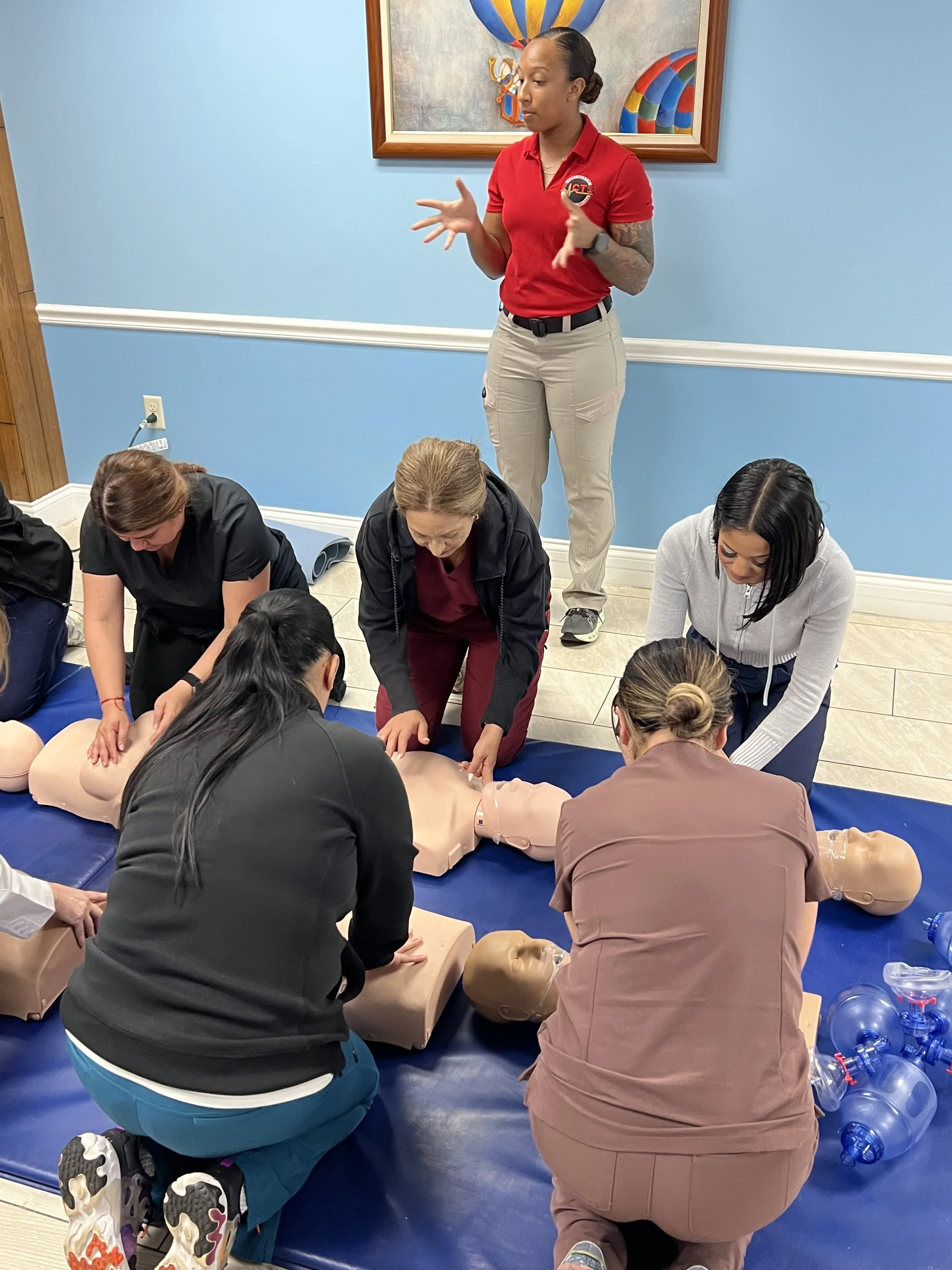 Instructora de FACTS supervisa a estudiantes mientras practican RCP con maniquíes durante una clase en español.