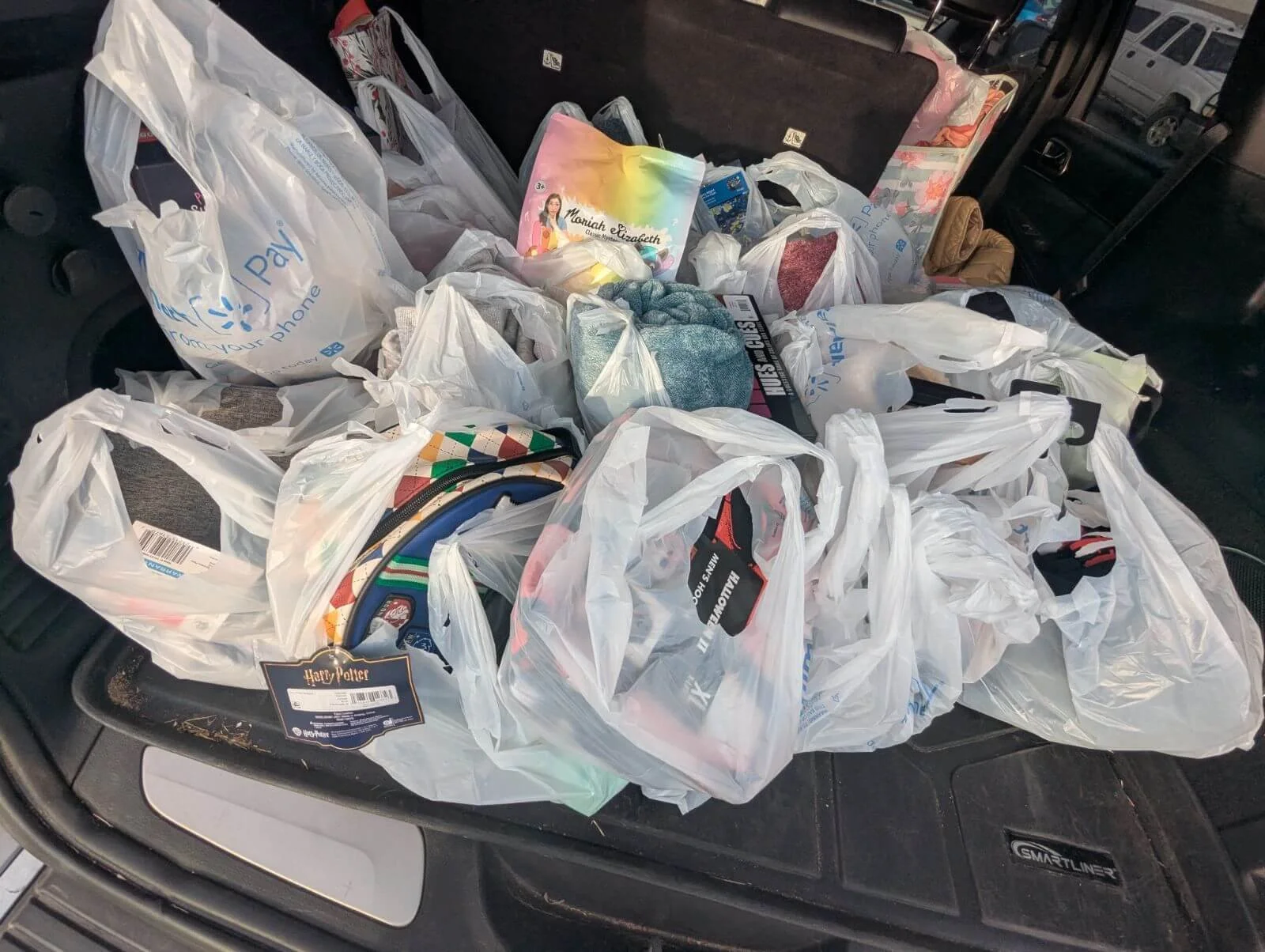 The image shows the back of a vehicle filled with numerous plastic shopping bags, some containing various items including a Harry Potter tag, clothes, and toys.
