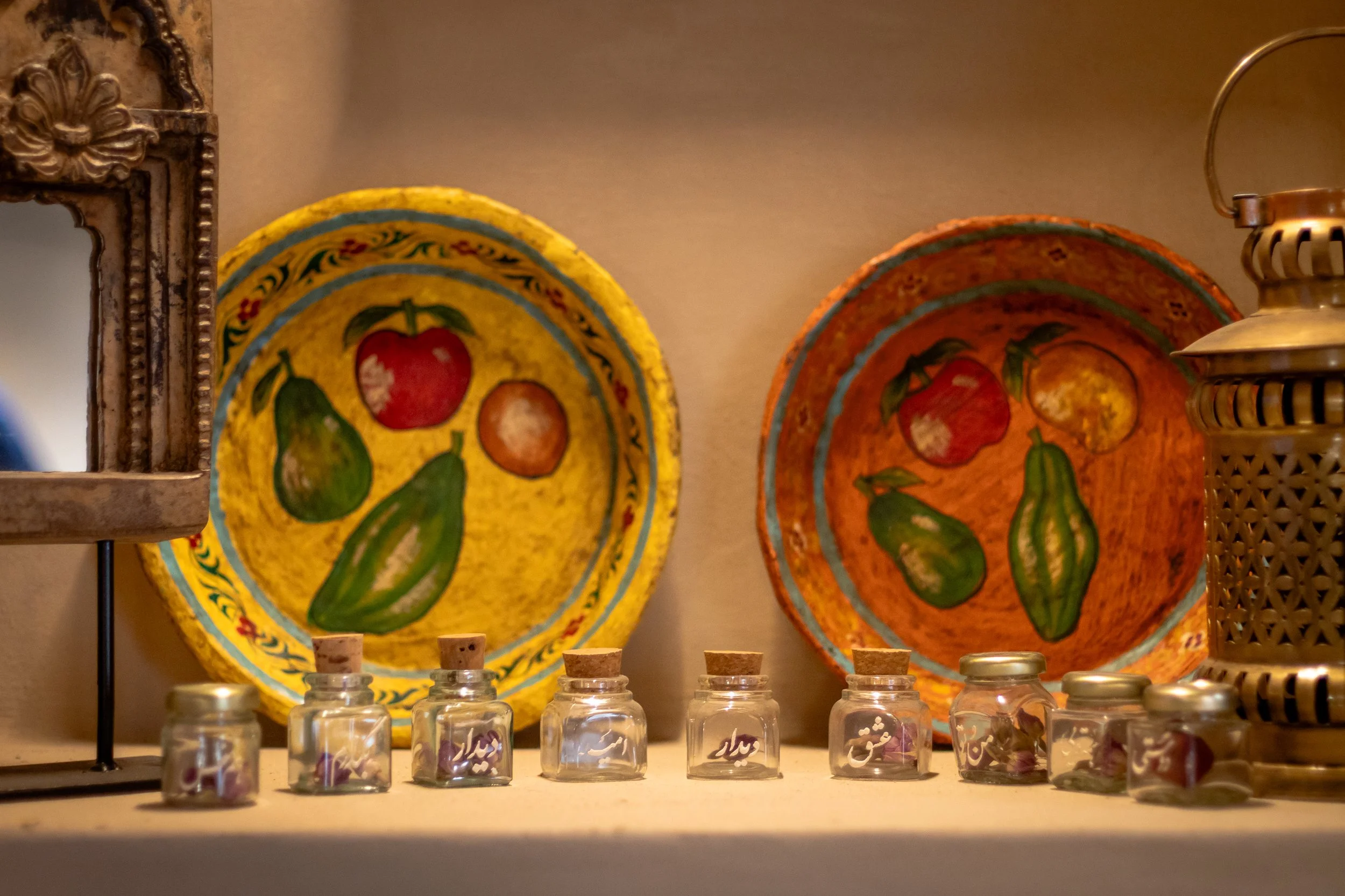 Colorful decorative plates with fruit designs, small glass jars with cork lids, and a metal lantern on a shelf.