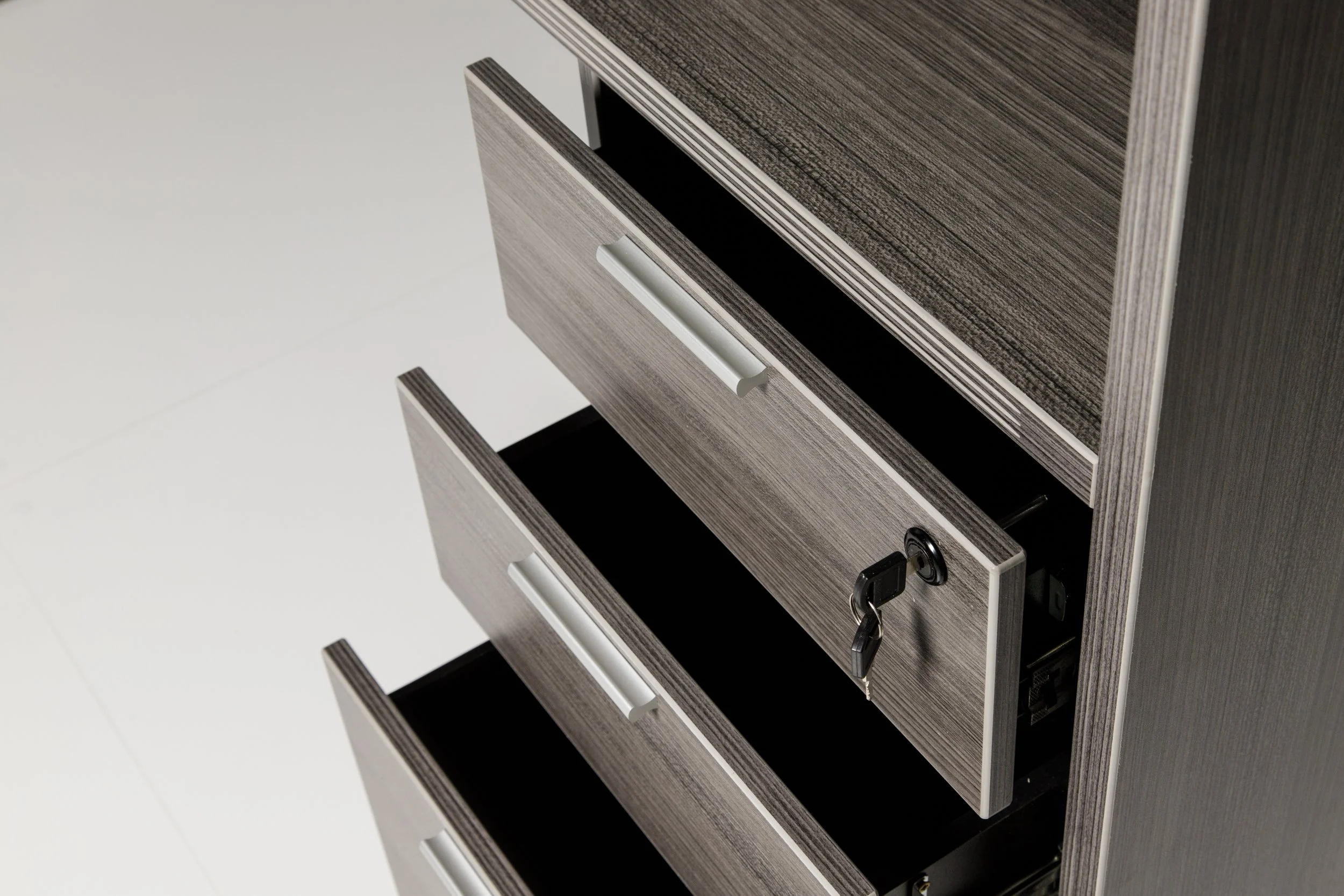 Three open drawers of a gray wood filing cabinet, with one drawer locked and a key hanging from it.
