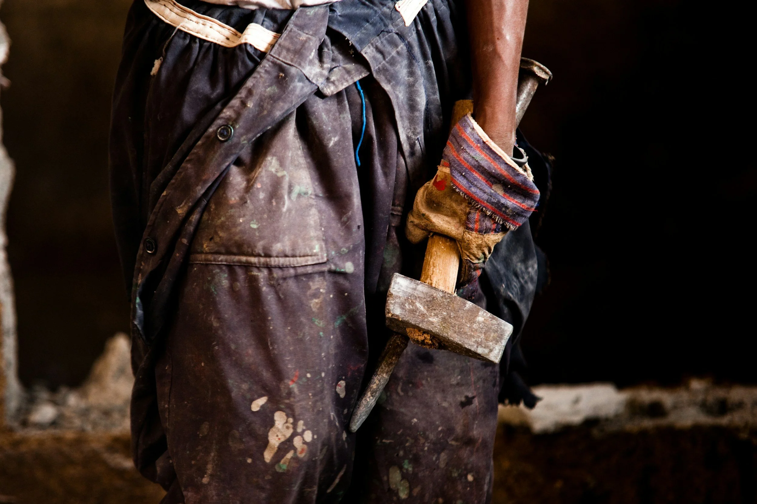 Persona con ropa de trabajo sucia, sosteniendo un martillo, en un ambiente de construcción o trabajo manual.