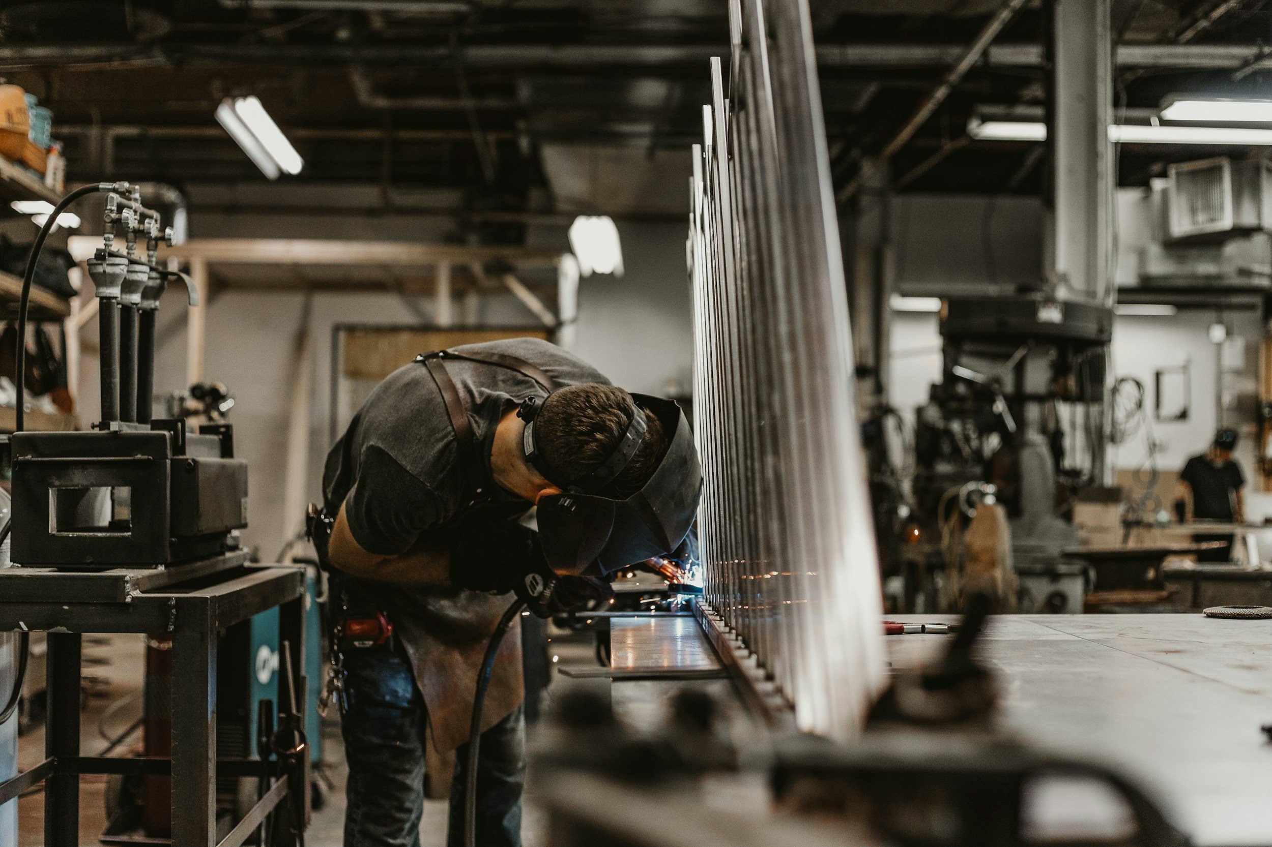 Una persona trabajando con equipo de soldadura en un taller de fabricación, rodeada de herramientas y estructuras metálicas.