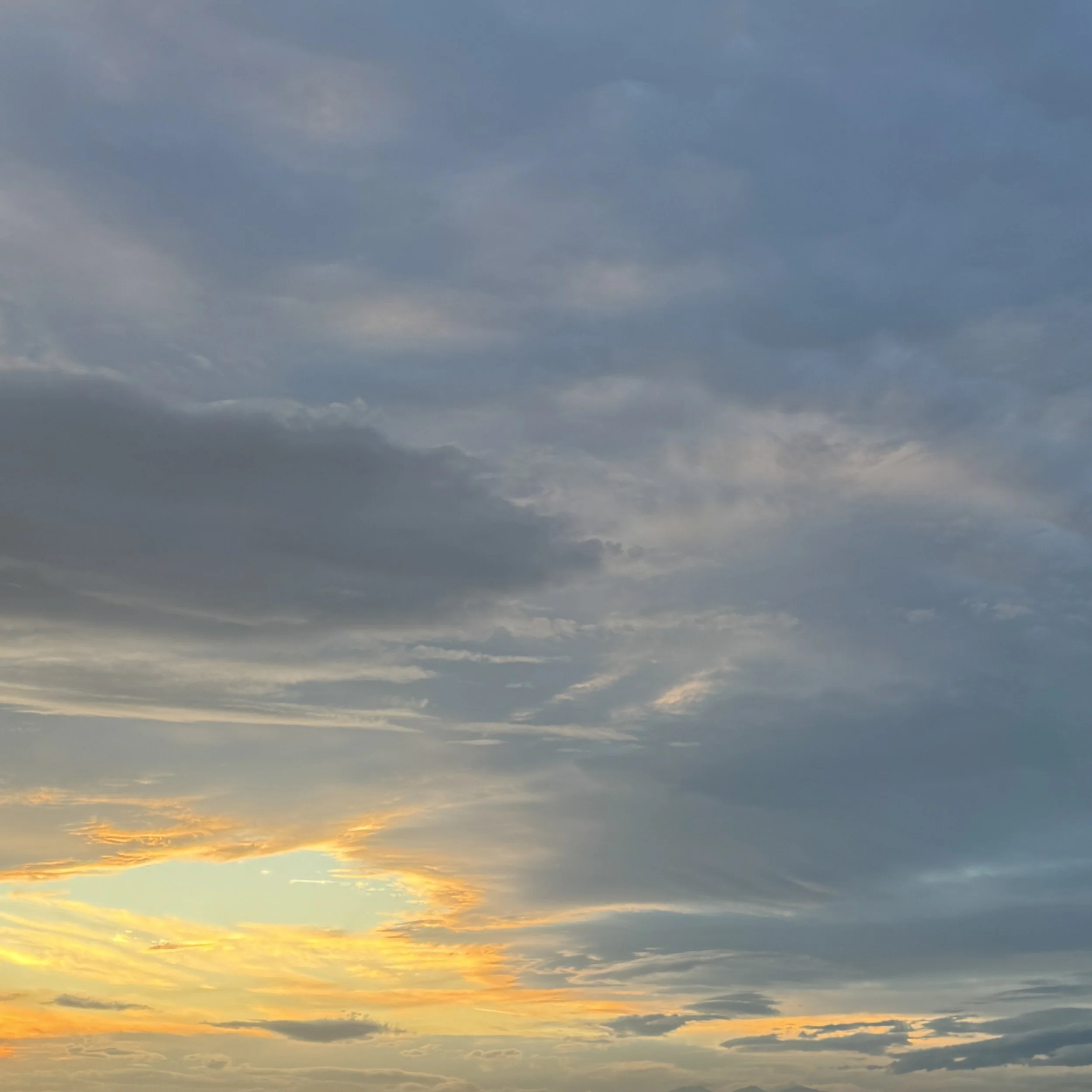 Cloudy sky during sunset with hues of yellow, orange, and blue.