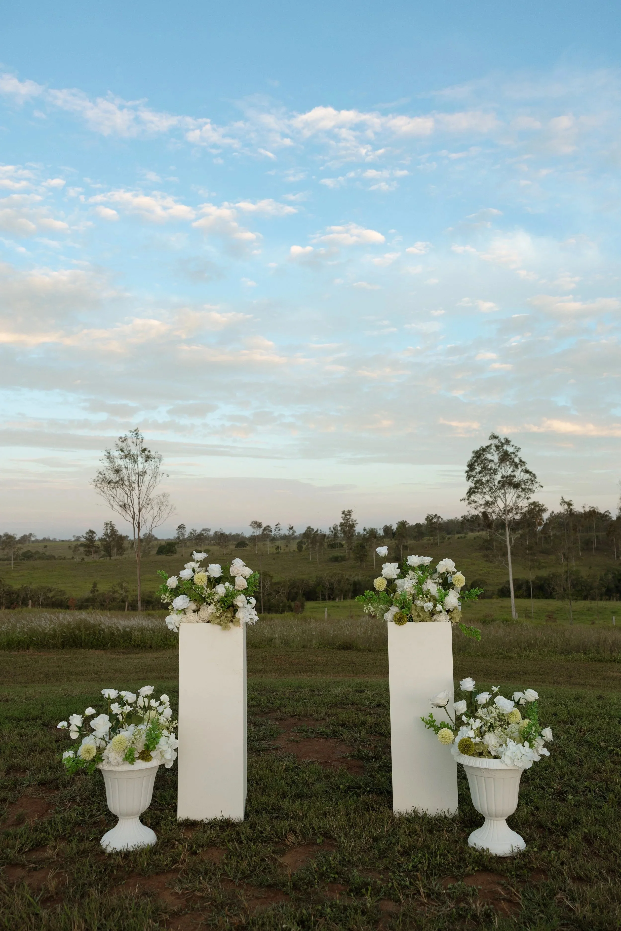 Luxury elopement ceremony styling in Hervey Bay with green and white floral arrangements on plinths and pots.
