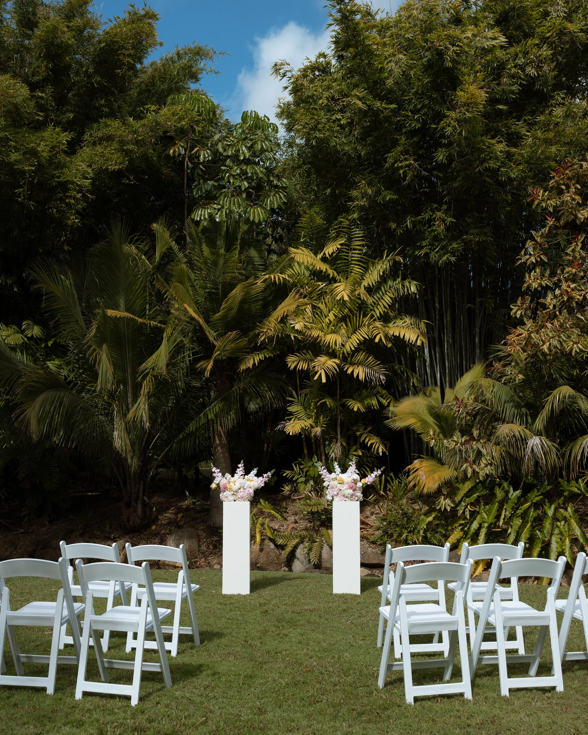All-inclusive elopement setup in Hervey Bay featuring colourful floral arrangements on plinths with ceremony chairs.