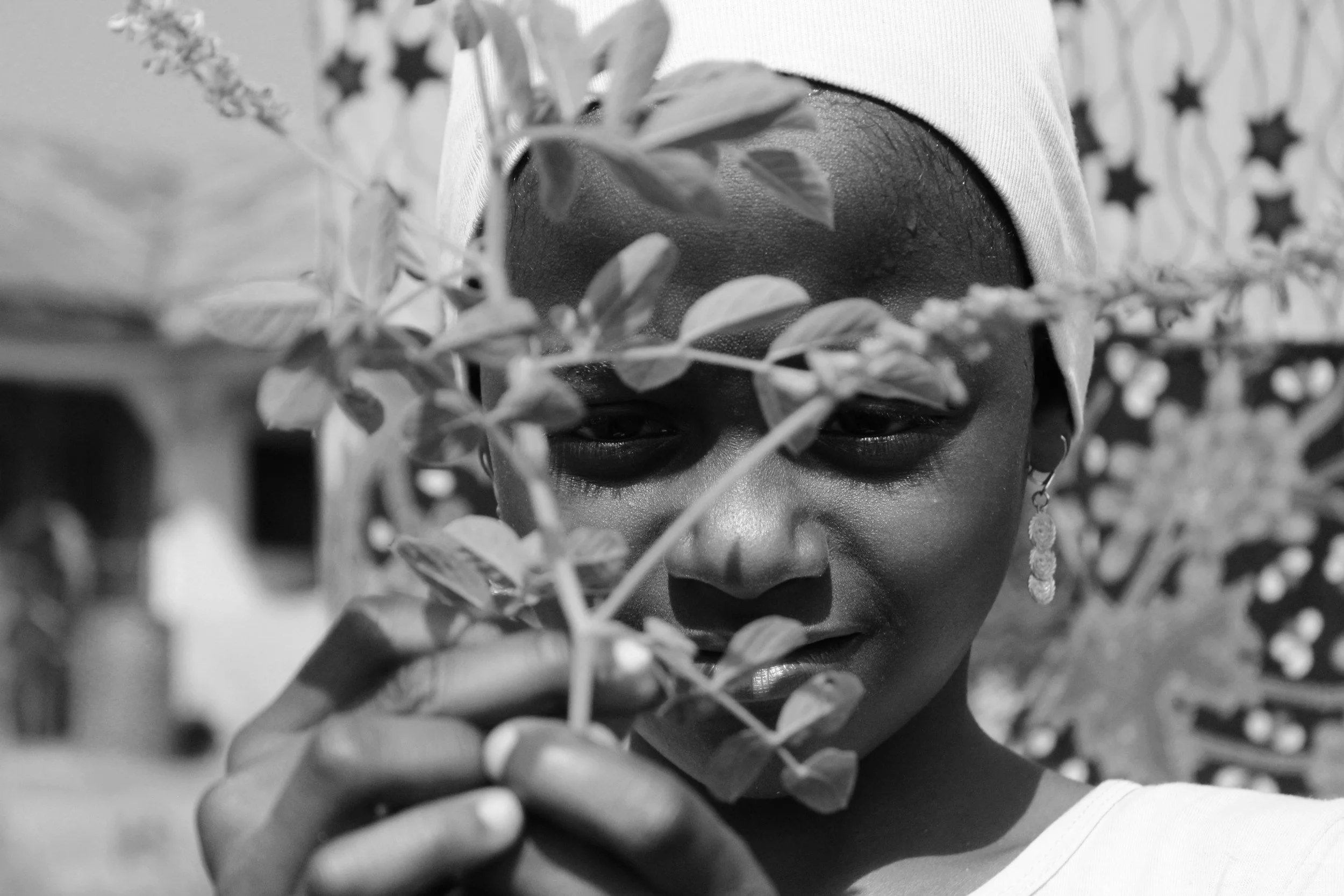 African American girl wearing a headscarf and earrings, holding an herbal plant branch close to her face, with a patterned background.