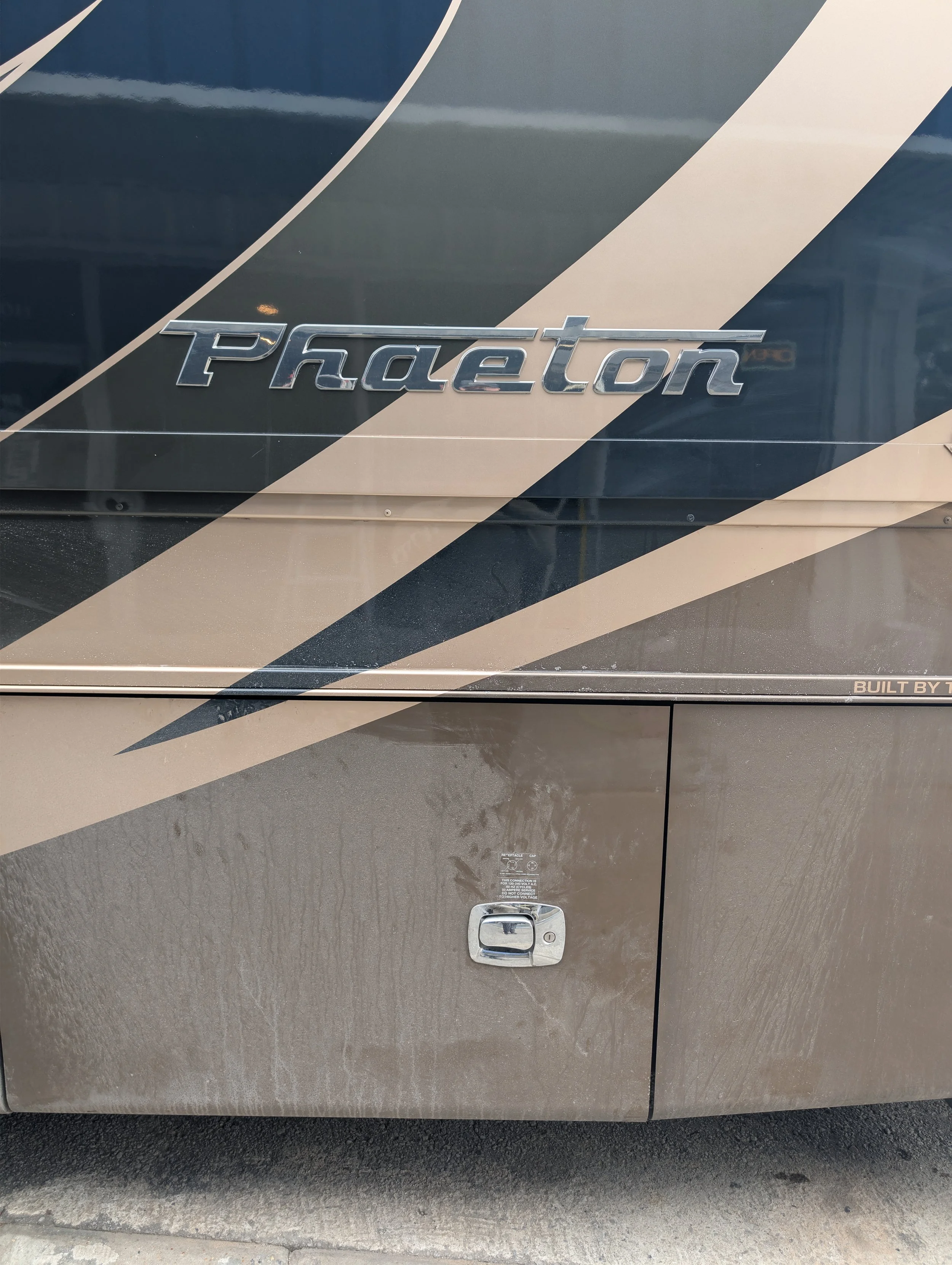 Close-up of the side of a Phaeton vehicle with a metallic badge, black and beige graphic design, and a storage compartment with a lock.