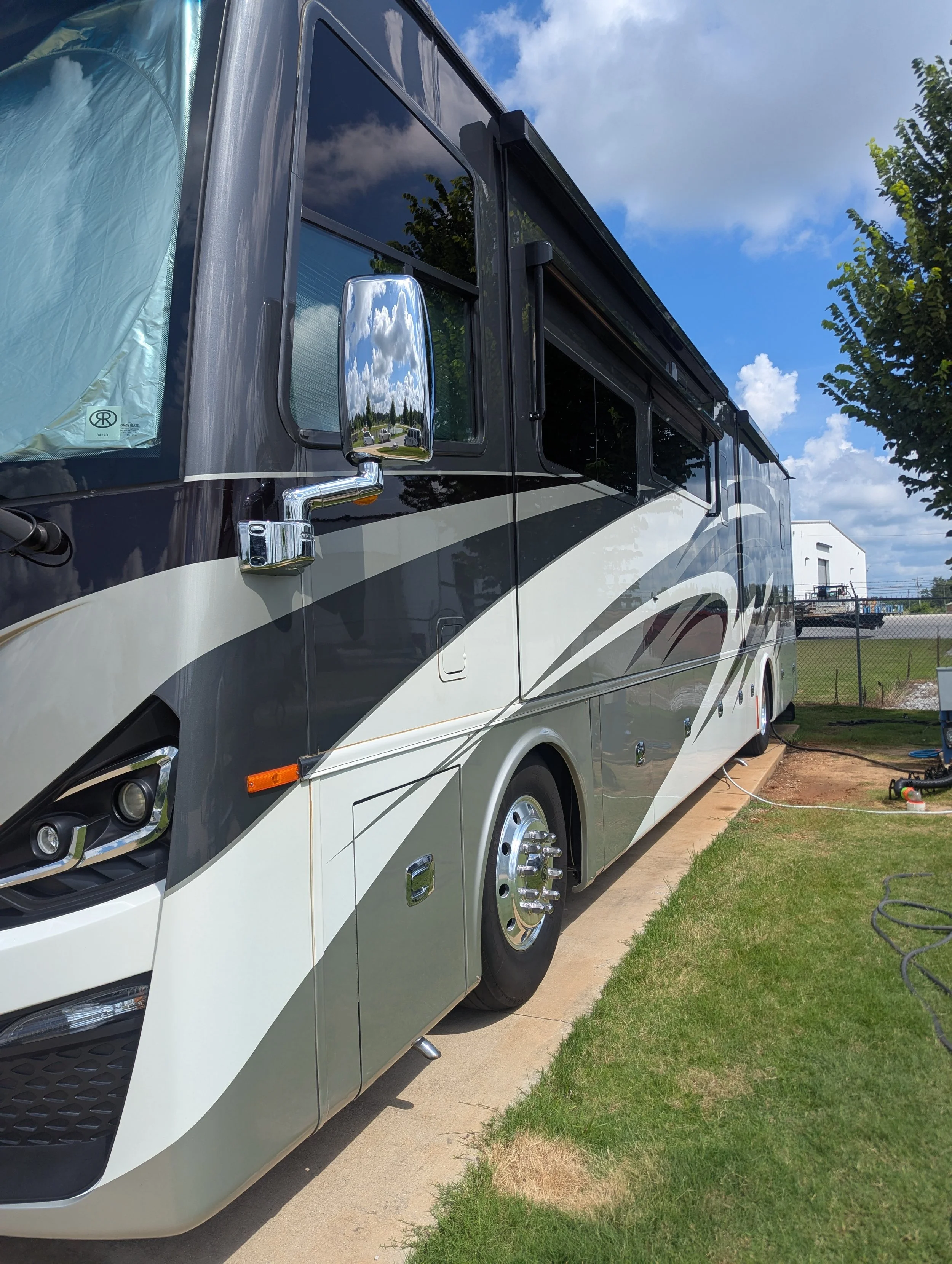 A black and white motorhome parked on a concrete pad next to a grassy area under a partly cloudy sky.