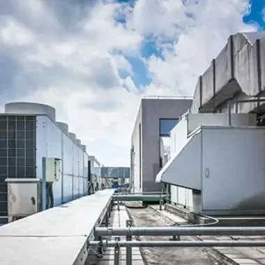 View of a rooftop with HVAC equipment, ducts, and pipes on a commercial building, under a cloudy sky.