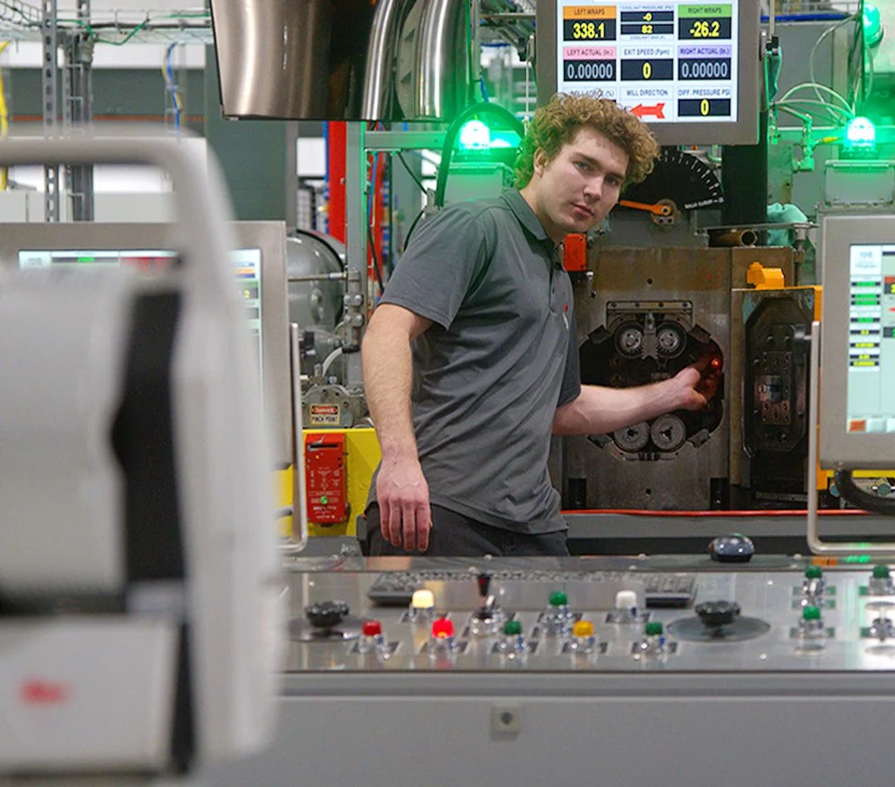 A man operating industrial machinery in a factory or control room with various digital displays and control panels.
