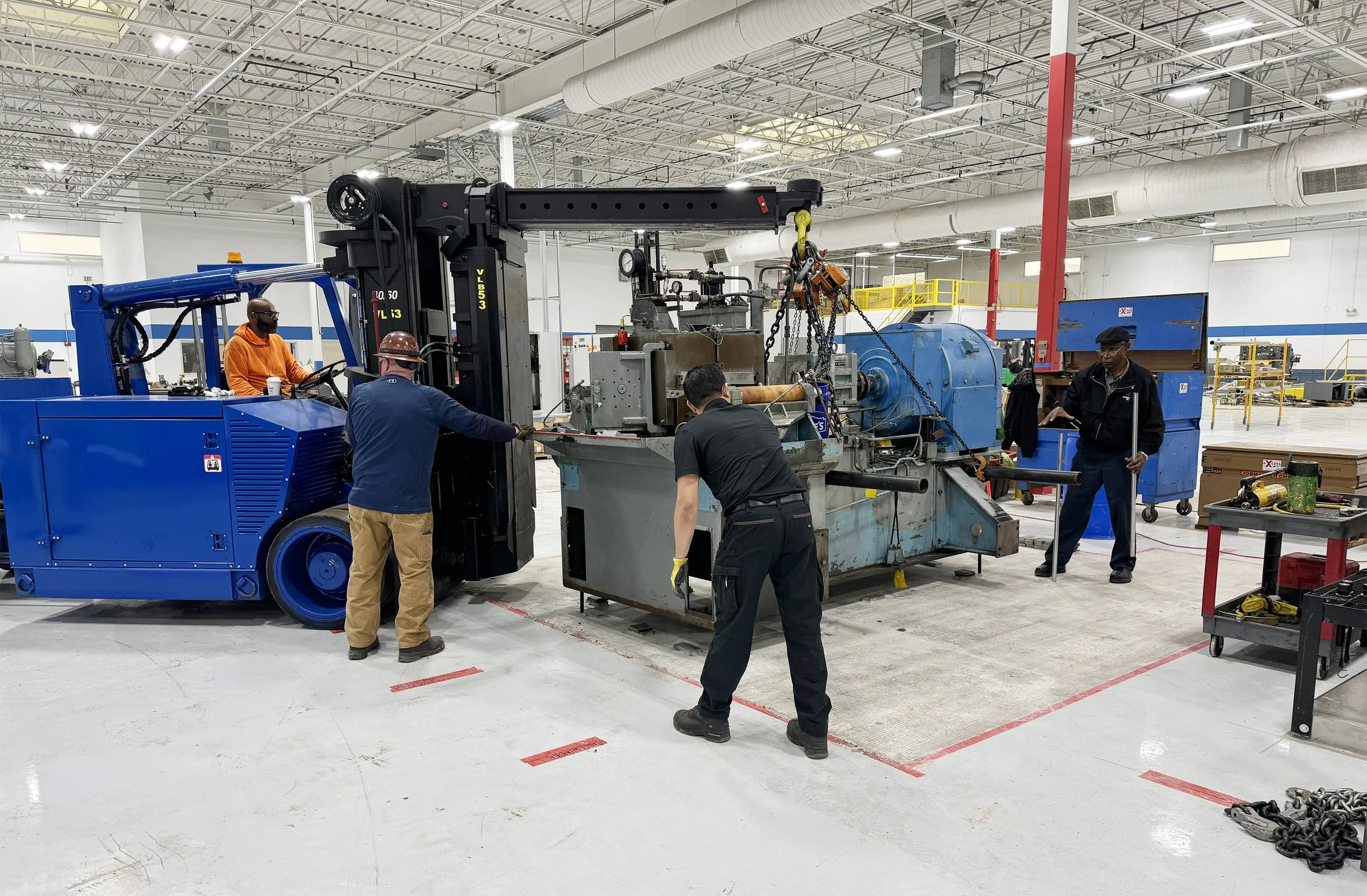 Workers operating and maintaining moving mills in an industrial factory, using tools and a blue forklift to handle large machinery with pressure gauges.