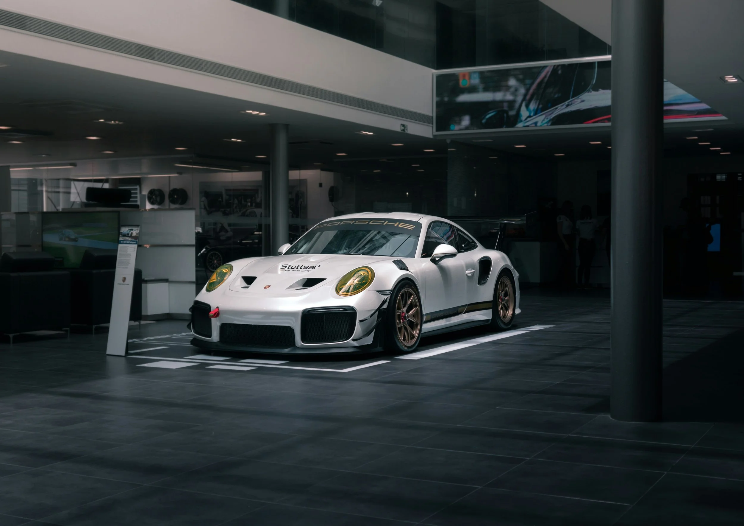 A white Porsche race car with gold wheels parked inside a showroom.