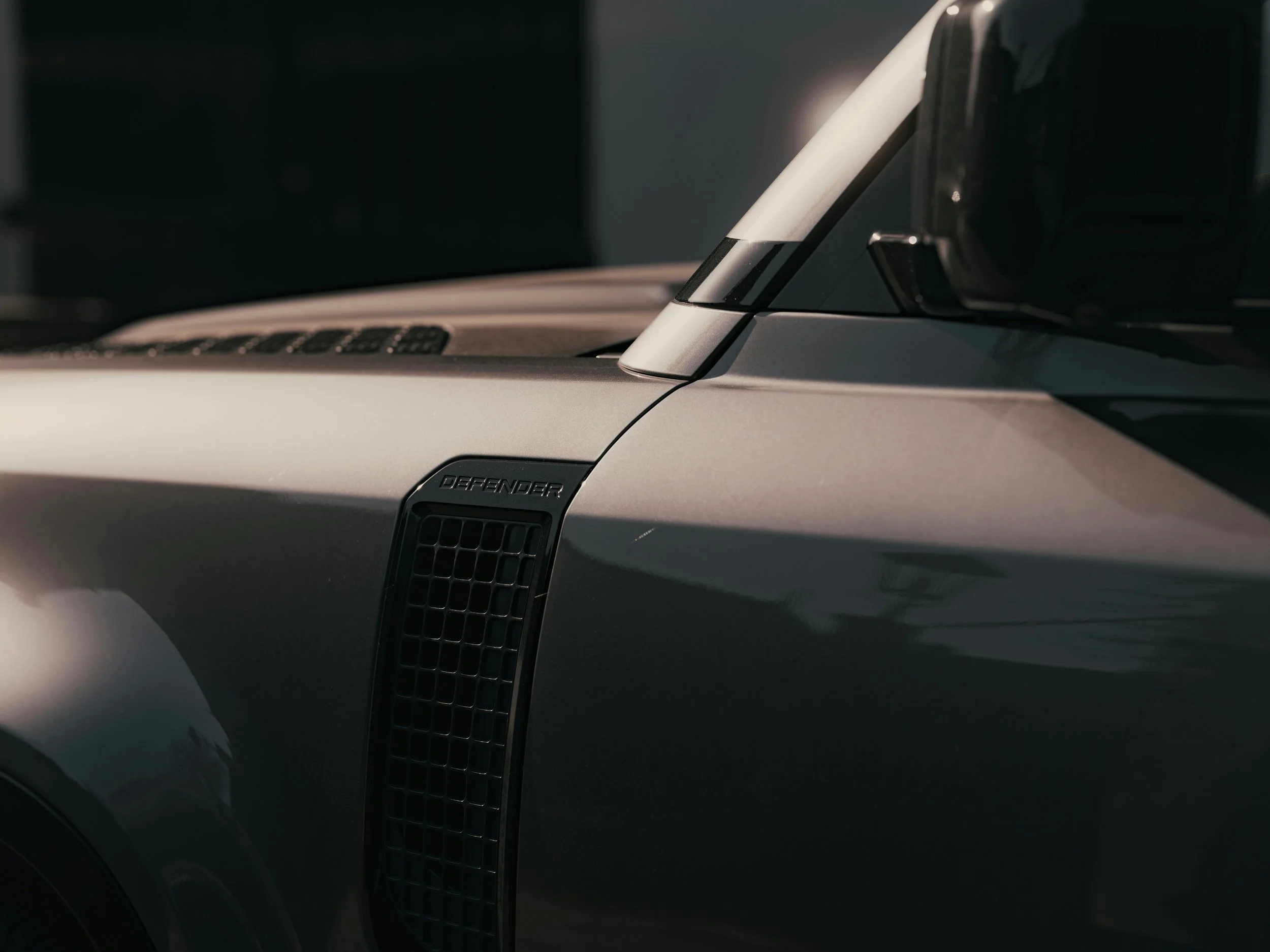 Close-up of a silver vehicle's front with black vents and the word 'Defender' on the side, showcasing a modern design.