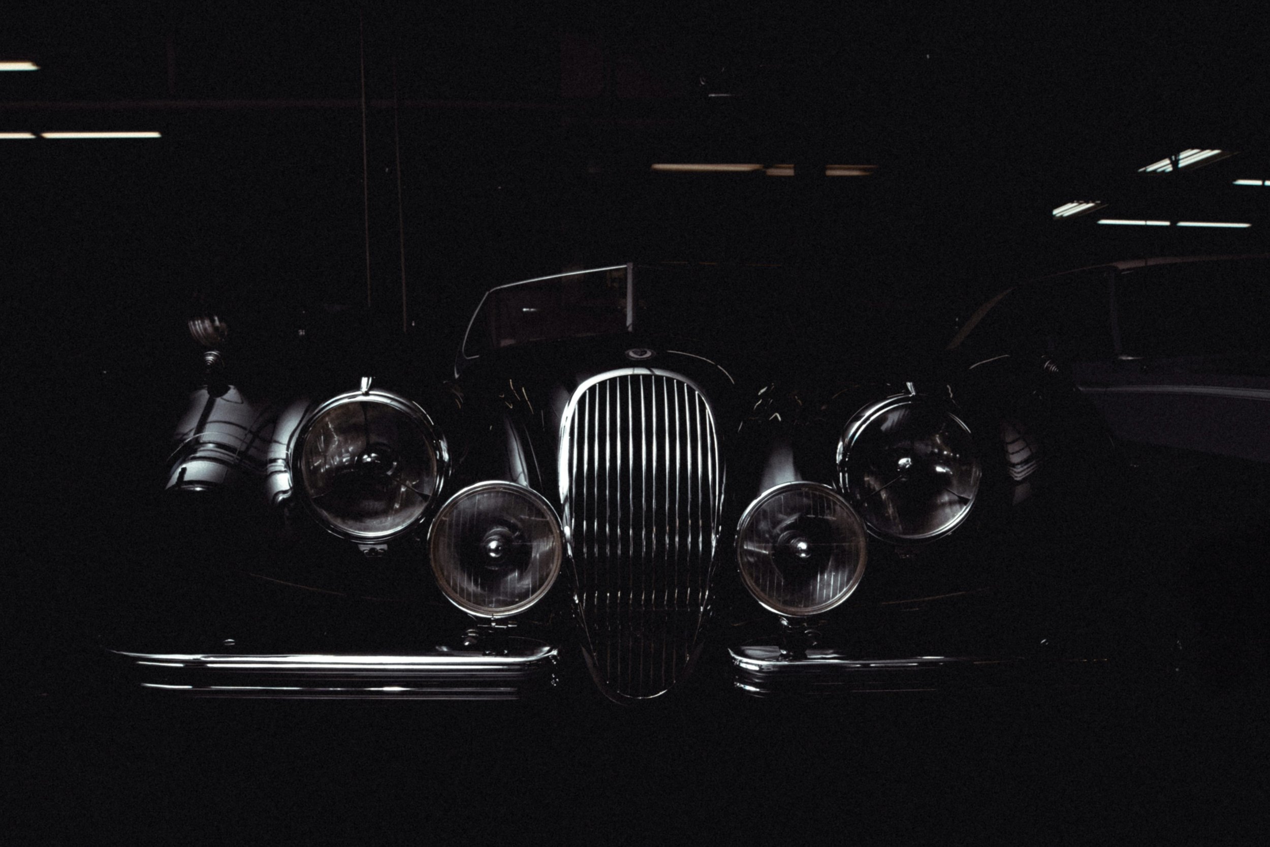 A vintage black luxury car with multiple headlights parked in a dark indoor showroom.