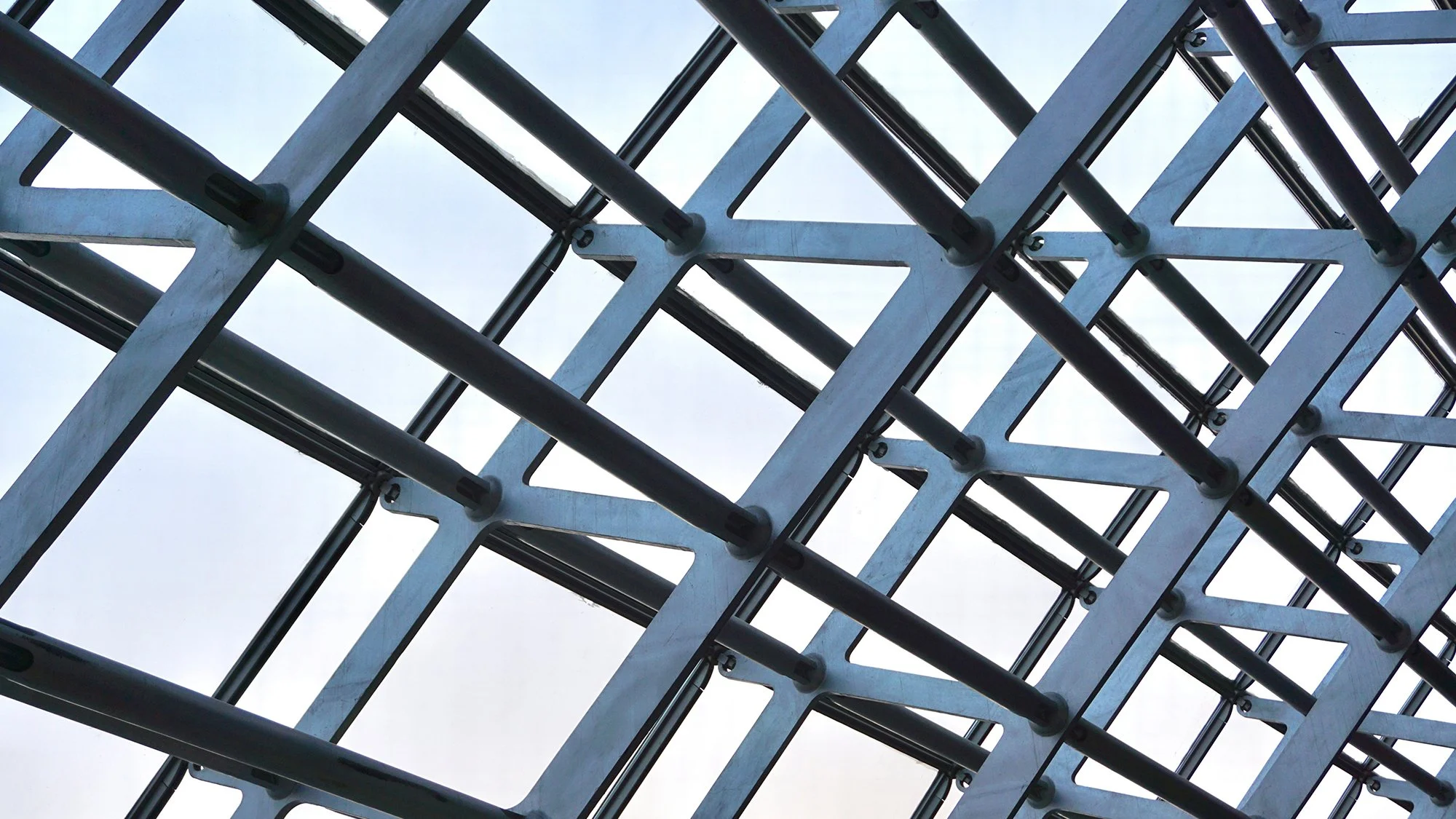 Geometric metal framework forming a repeating grid pattern against a pale sky.
