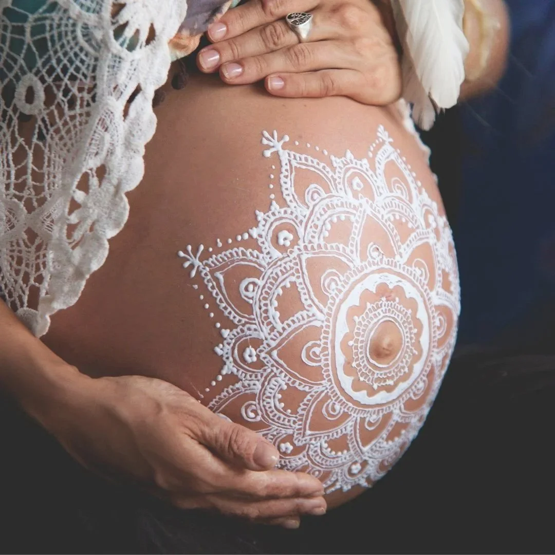 Pregnant woman's belly decorated with white henna mandala design.