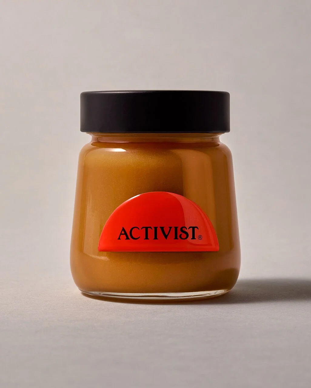 A small jar of Activist brand peanut butter with a black lid and a red label.