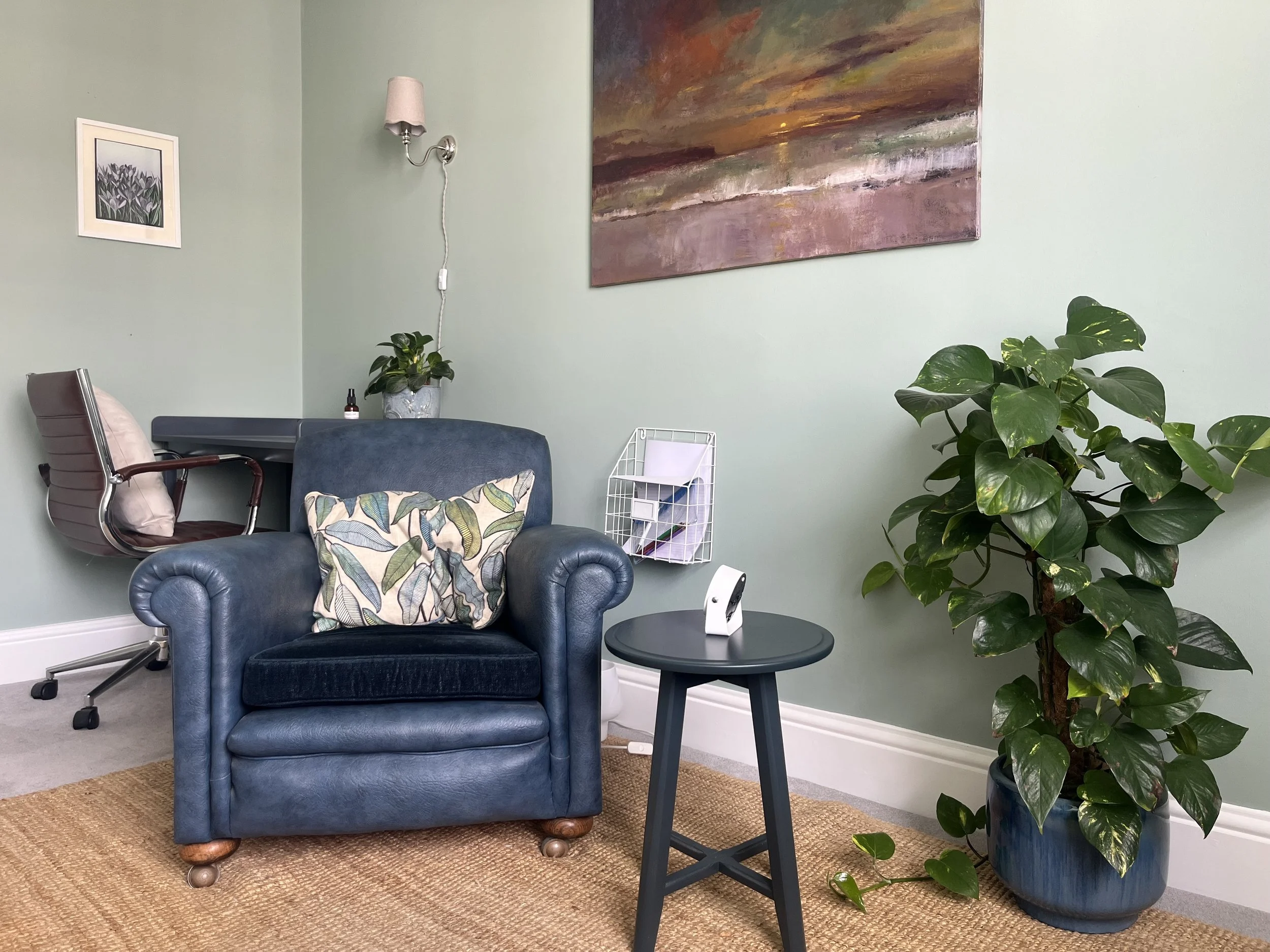 Welcoming counselling room in Cheltenham with a blue armchair, soft furnishings and houseplants.