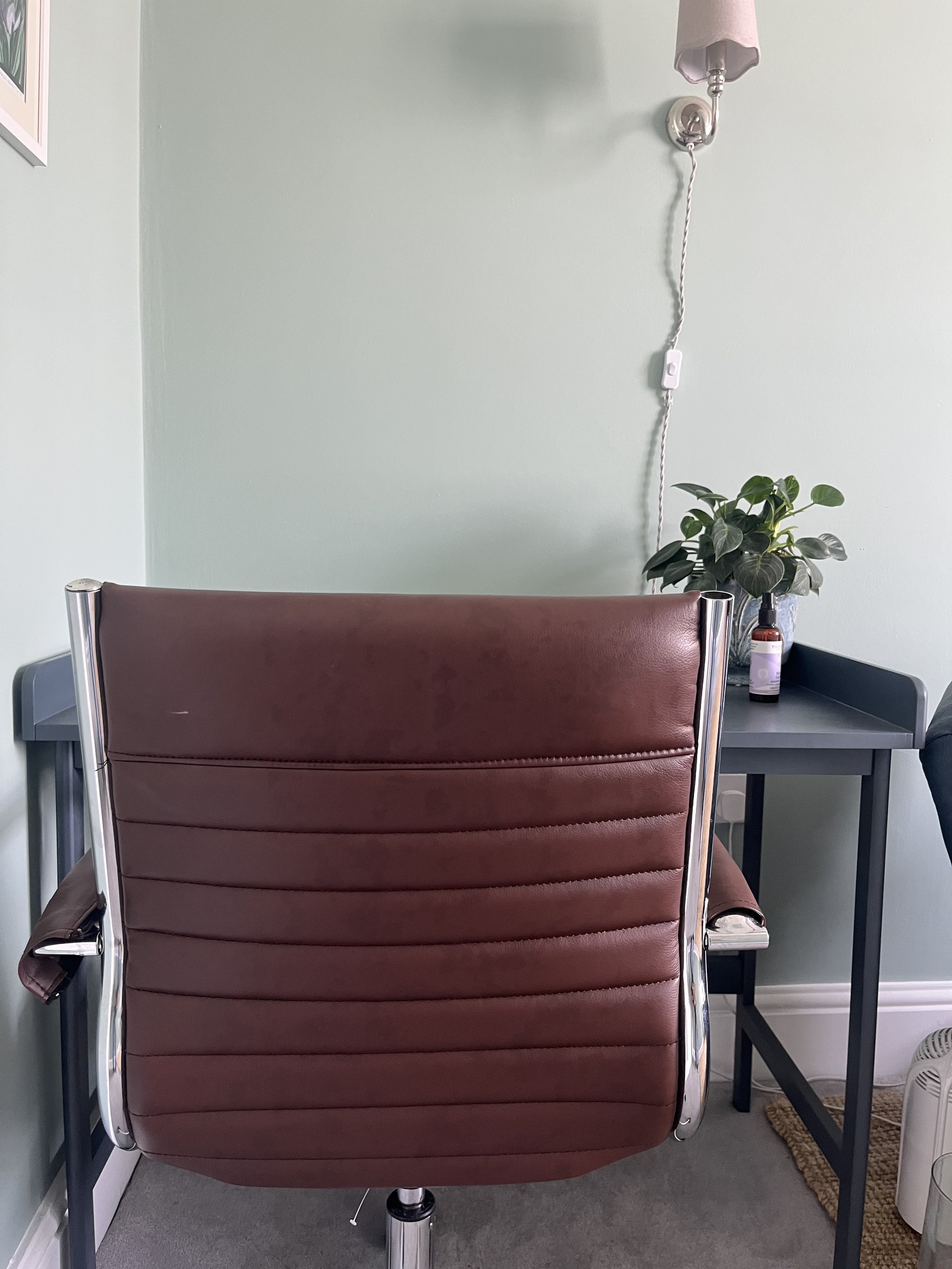 Welcoming counselling room in Cheltenham with a comfortable brown leather chair and a leafy plant.