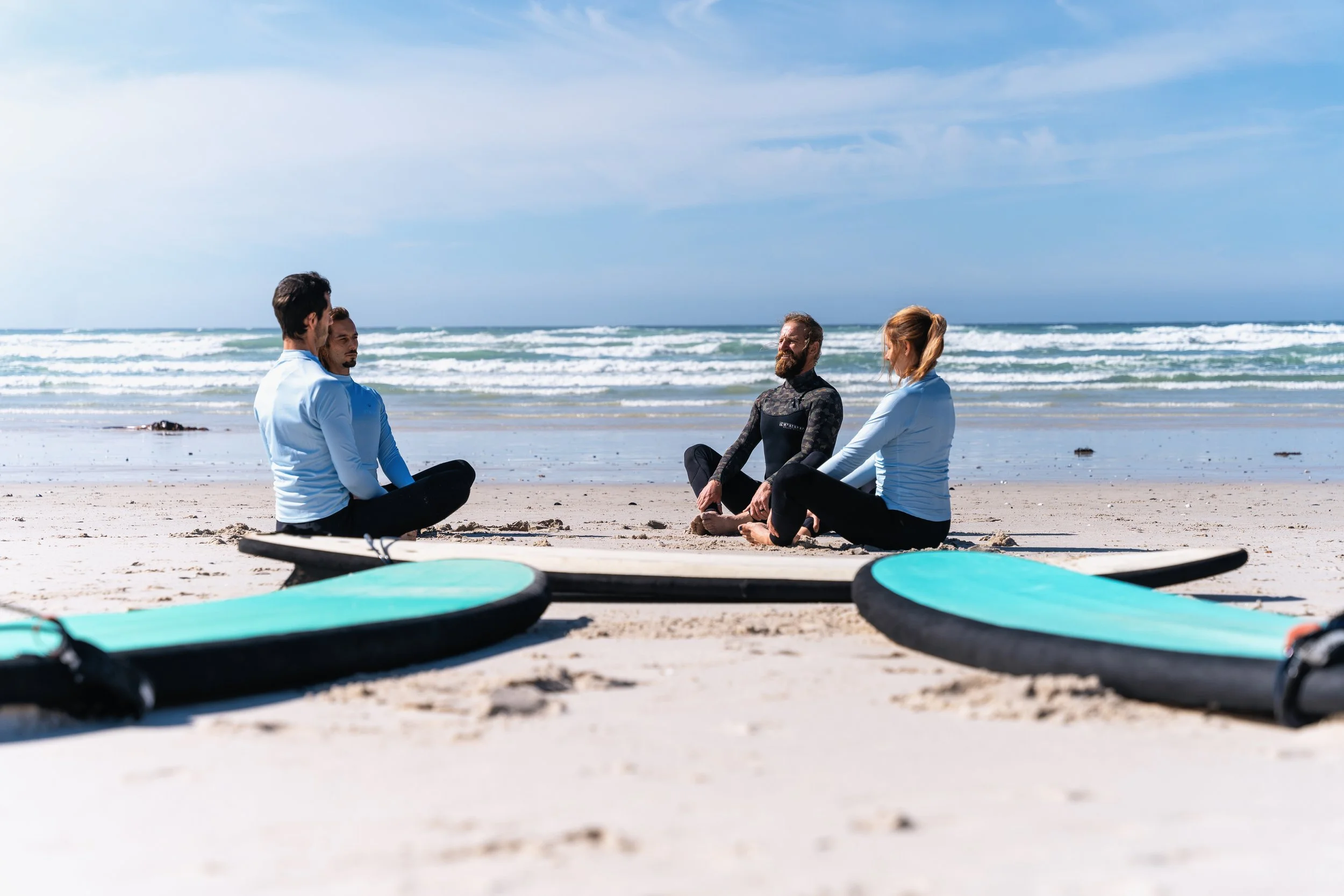 Saltwater Souls surf instructor and students sitting together on the beach with surfboards, chatting before a lesson in Cape Town