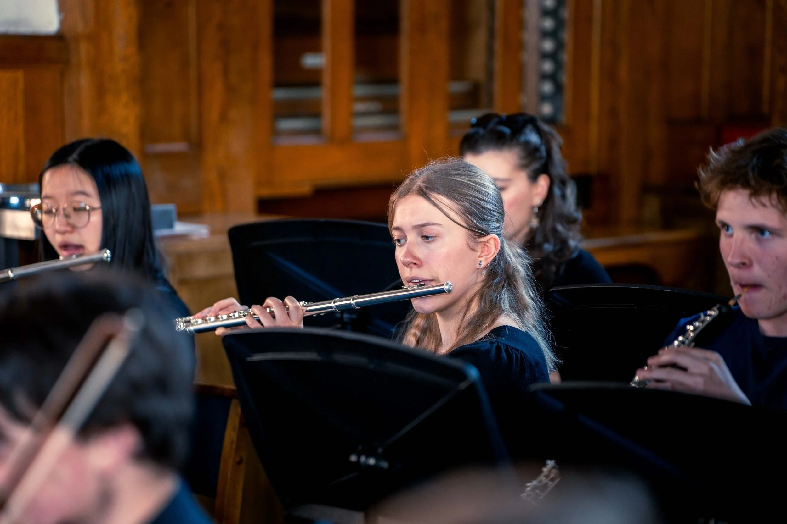 Young musicians playing wind instruments in an orchestral concert with a wooden background.