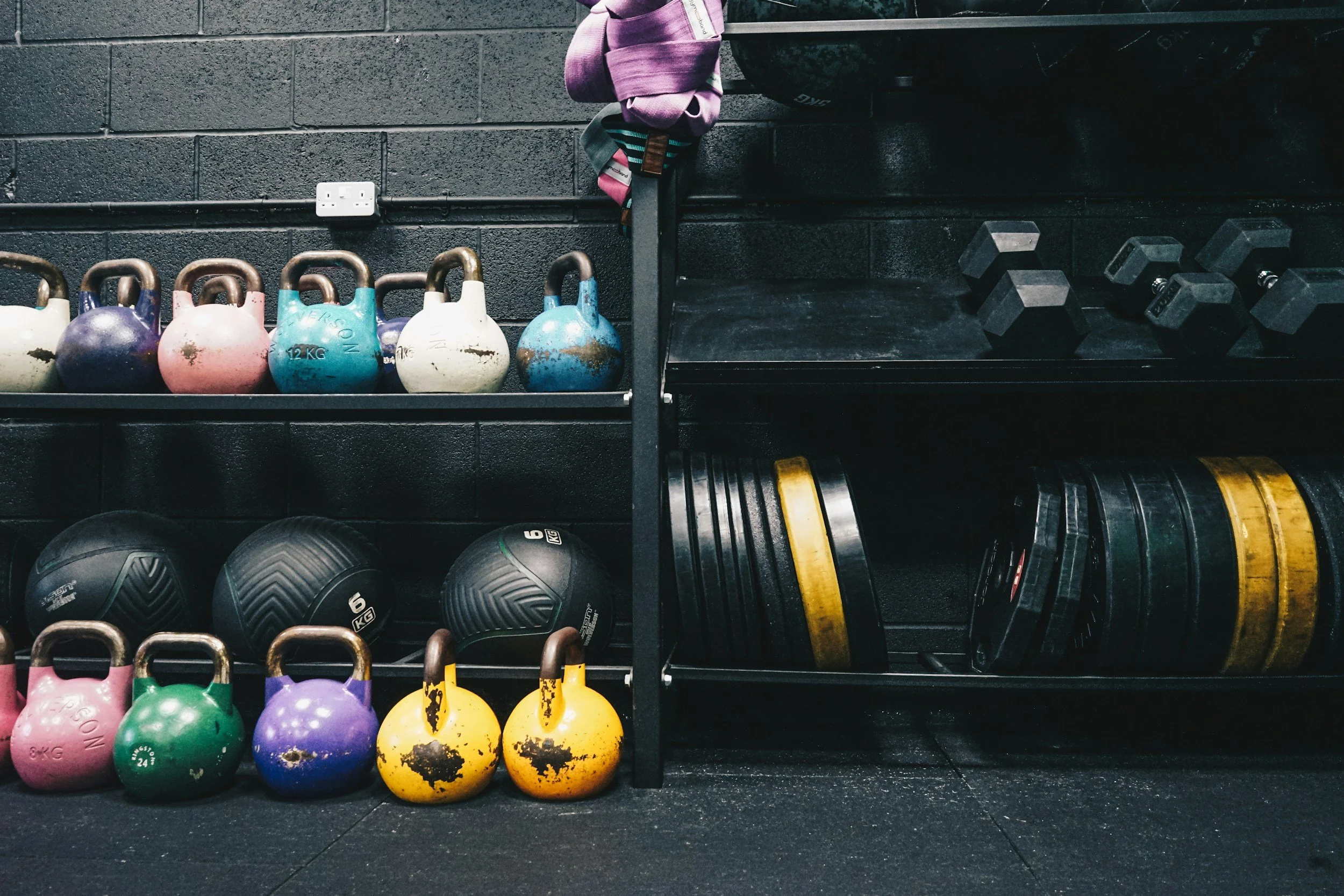 Wall-mounted shelves in a gym store holding kettlebells, dumbbells, and weight plates.