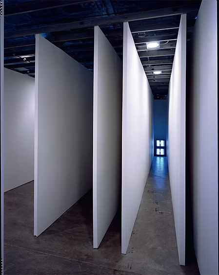 Gallery with tall, white partition walls forming narrow pathways