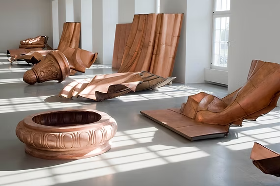 Artistic wooden sculptures displayed in a bright gallery space with sunlight streaming through large windows.