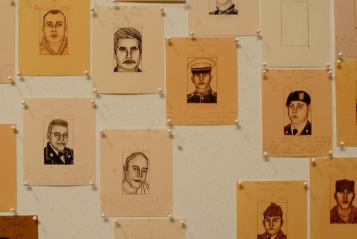 A wall display of various vintage sketches and photographs of men, pinned to a white board with thumbtacks.