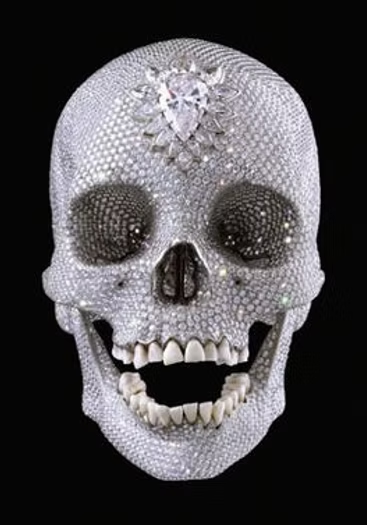A skull decorated with numerous small diamonds or rhinestones, featuring dark eye sockets and a large central gem on the forehead, set against a black background.
