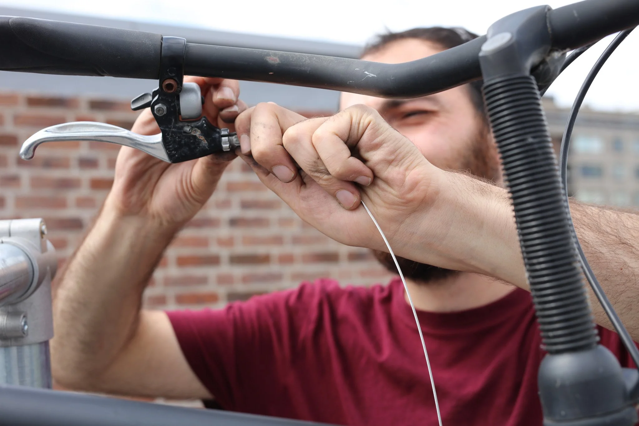 Een man die een fiets afstelt of repareert op een buitenlocatie met een bakstenen muur op de achtergrond.