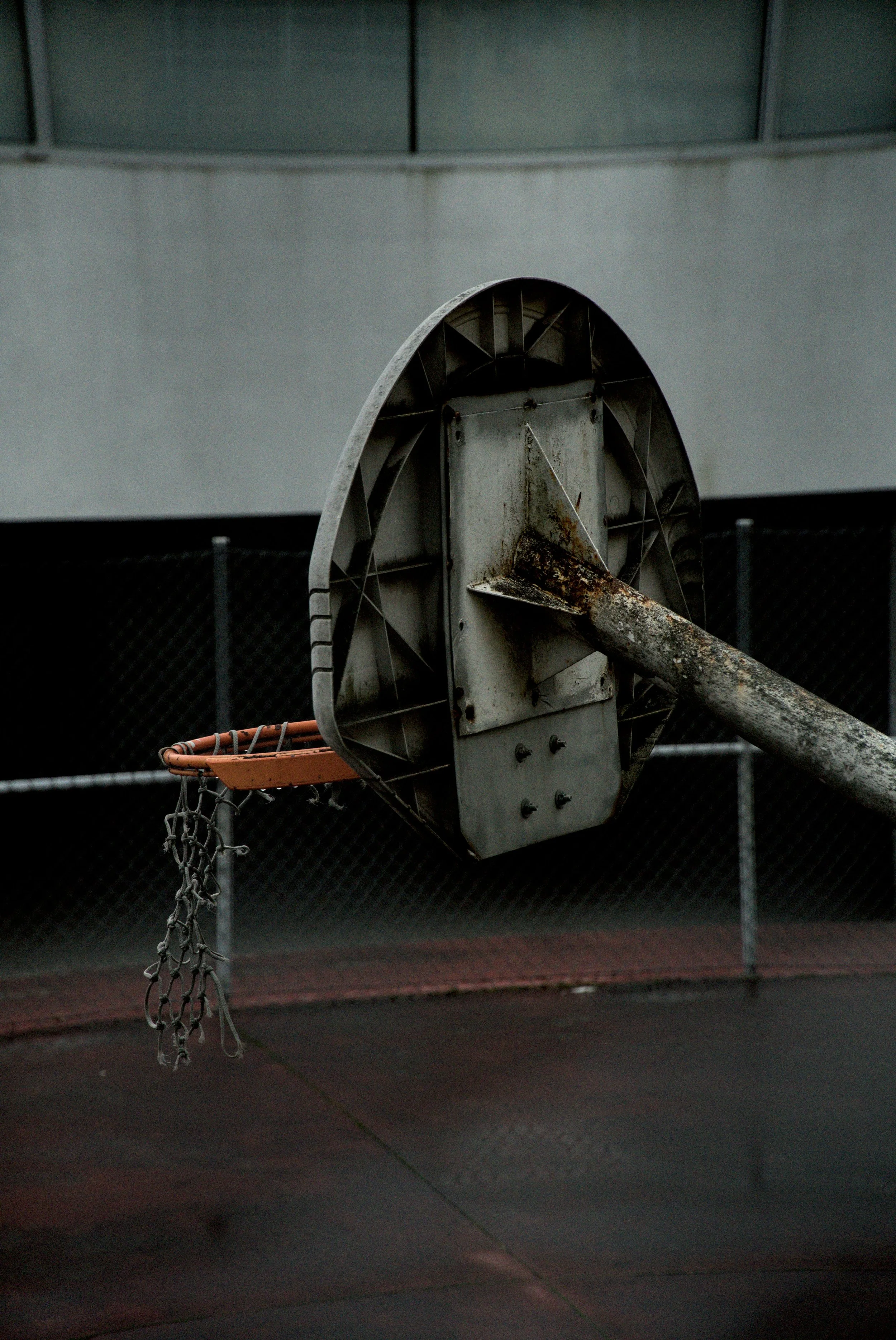 Old basketball hoop with rusty backboard and chain net, located outdoors on a sports court.