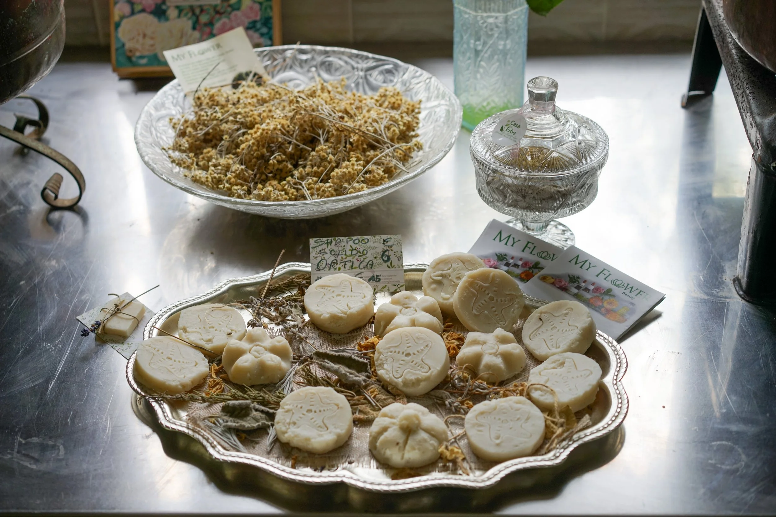 Biscotti artigianali decorati con stelle, vasetti di cristallo e piatti con fiori secchi, in un ambiente luminoso.
