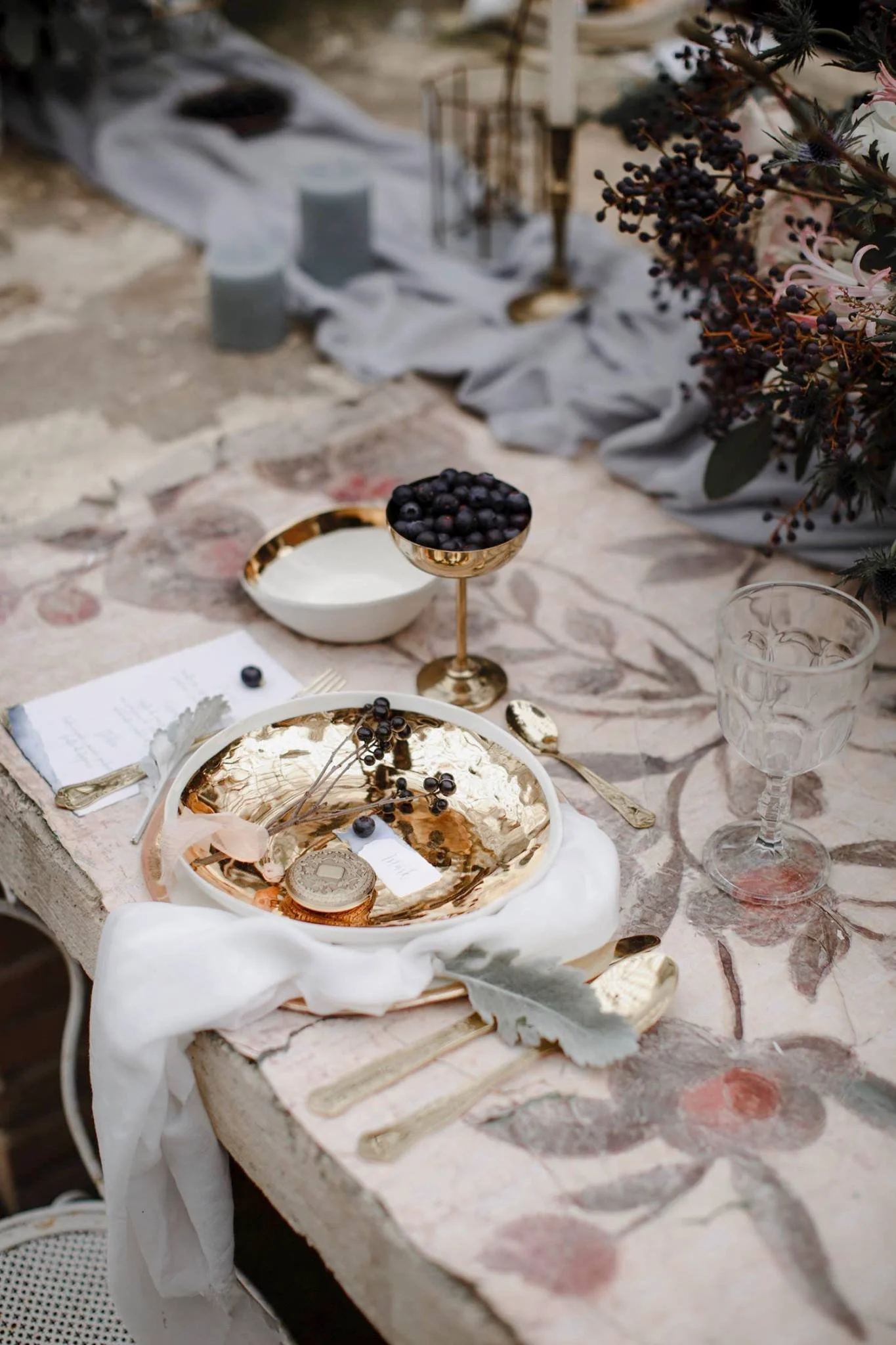 Tavola elegante apparecchiata con piatti e bicchieri decorativi, decorazioni floreali e bacche di piante, per un evento speciale.