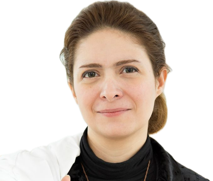 Close-up of a woman with light brown hair, fair skin, smiling gently, wearing a black turtleneck and white jacket against a plain background.