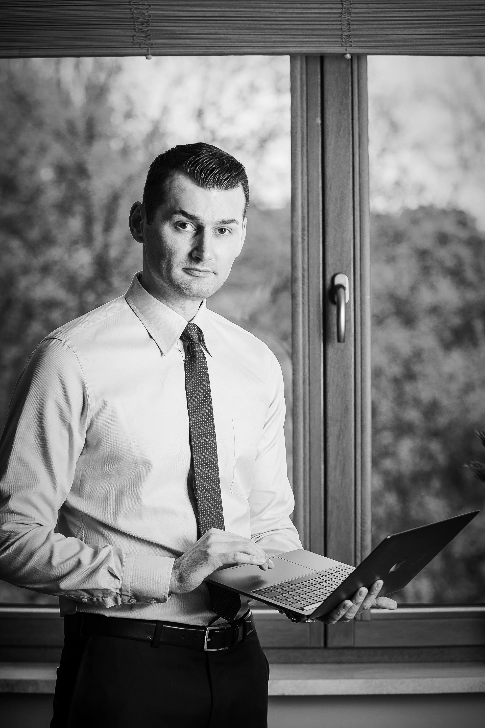 Black-and-white portrait of Artur Sinderman, founder of ASI.studio. An IT and AI consultant holding a MacBook, representing professional technology consulting, process automation, and online business consultations.