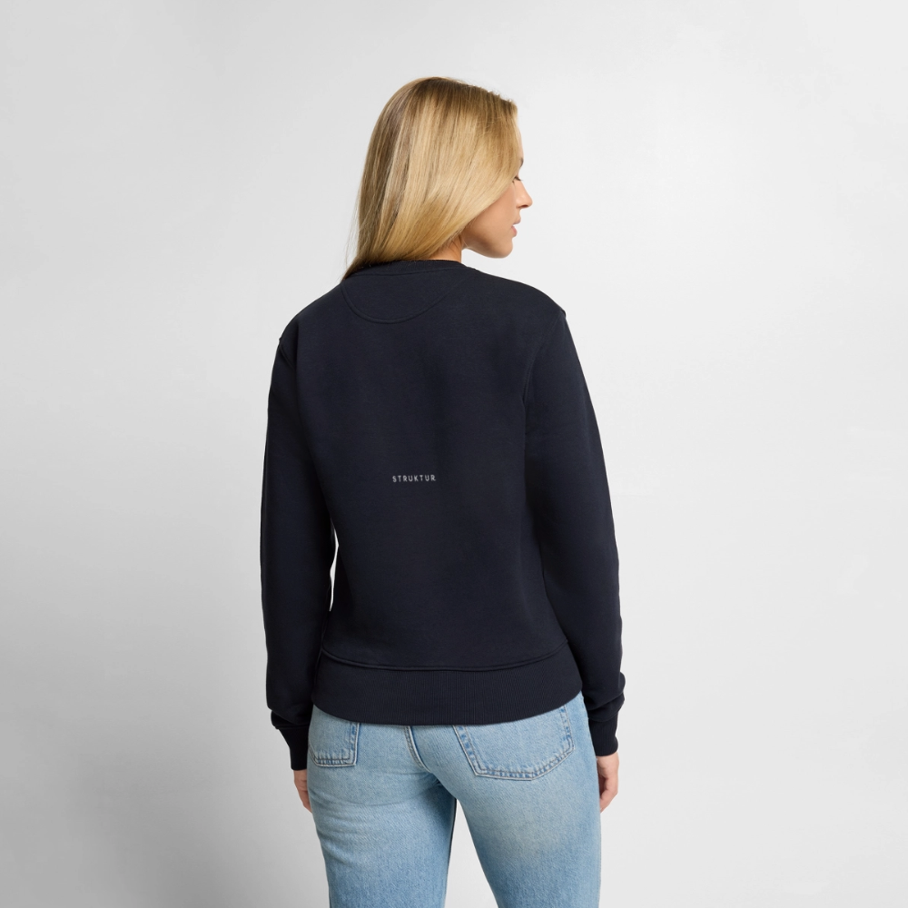 Kvinde i blå sweatshirt, set fra ryggen, med ordet 'STRUKTUR' på ryggen, og iført lyseblå jeans, står foran en hvid baggrund.