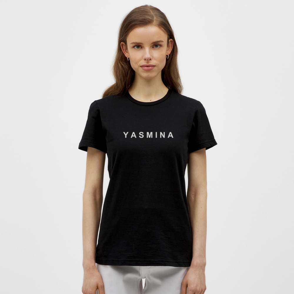 En kvinde med langt brunt hår iført en sort T-shirt med teksten 'YASMINA' på fronten, står foran en hvid baggrund.